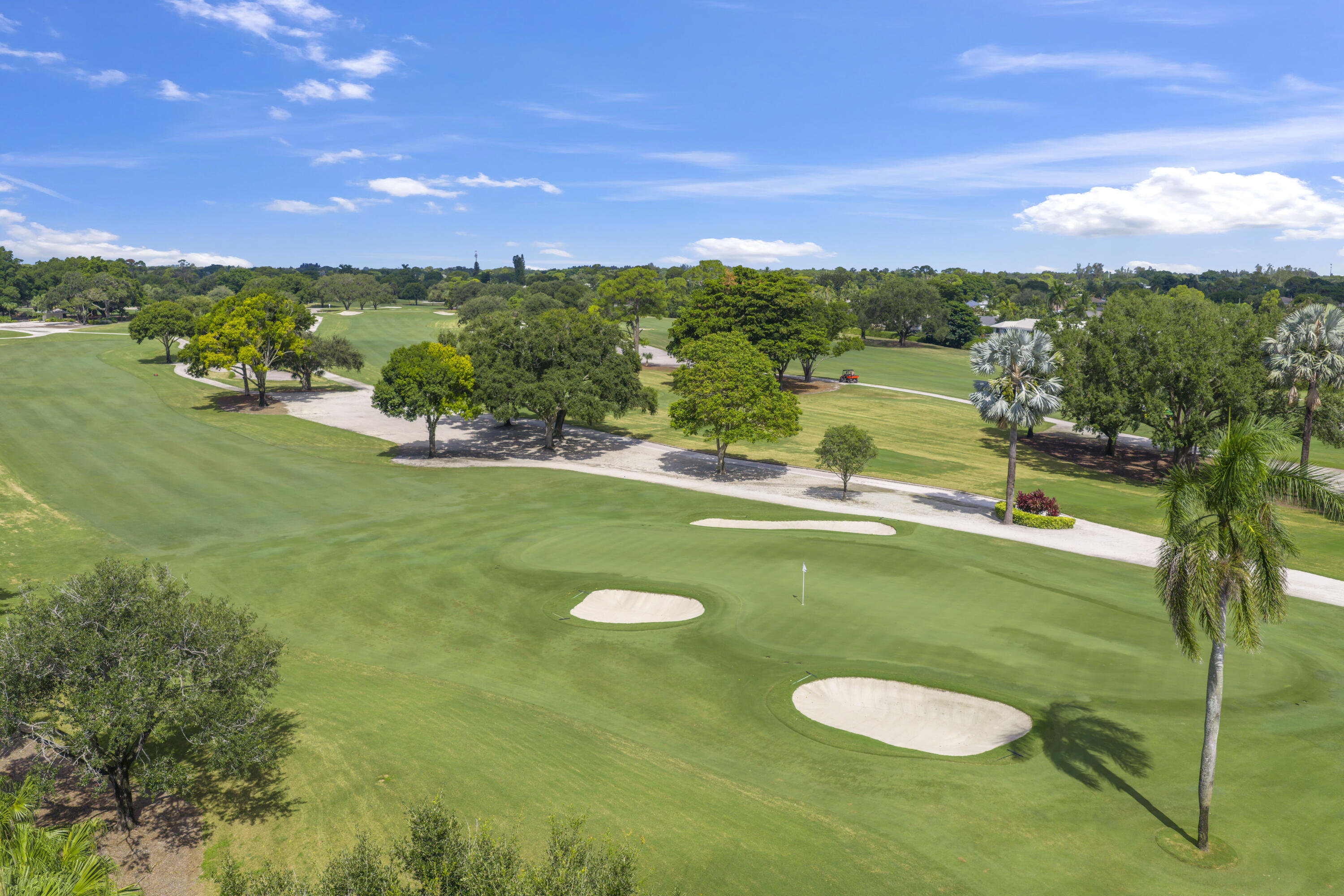 Expansive golf course grounds featuring multiple sand bunkers, manicured fairways, mature canopy trees, and ornamental palms