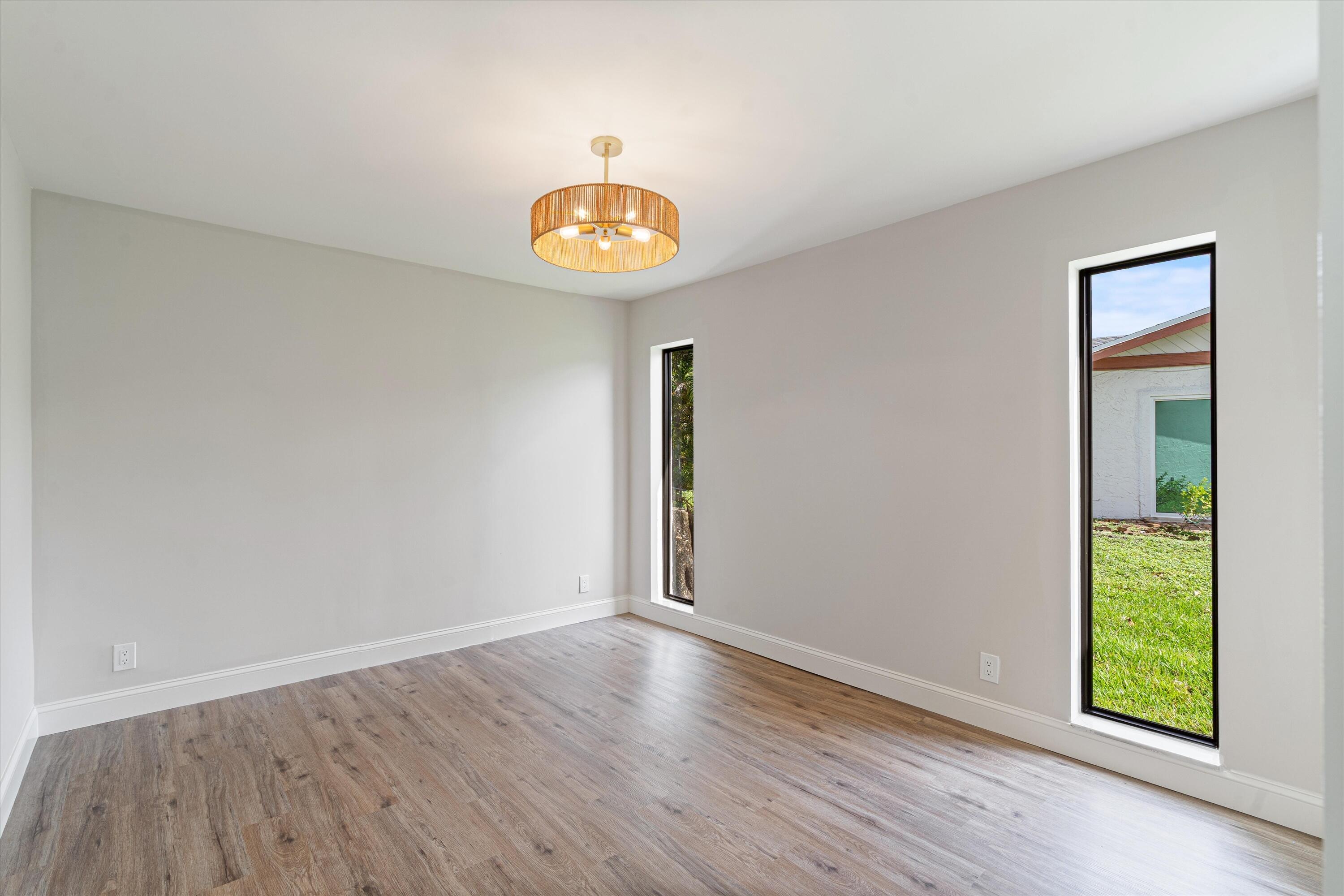 Neutral-toned room featuring wood-finish flooring, two vertical windows with black frames, and a drum-style pendant light fixture