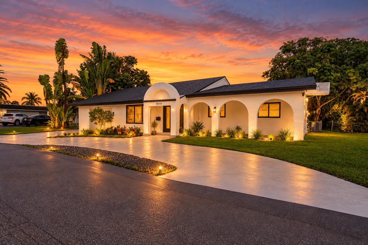Single-story exterior featuring a rounded arched portico, stucco facade, expansive concrete driveway, and manicured lawn