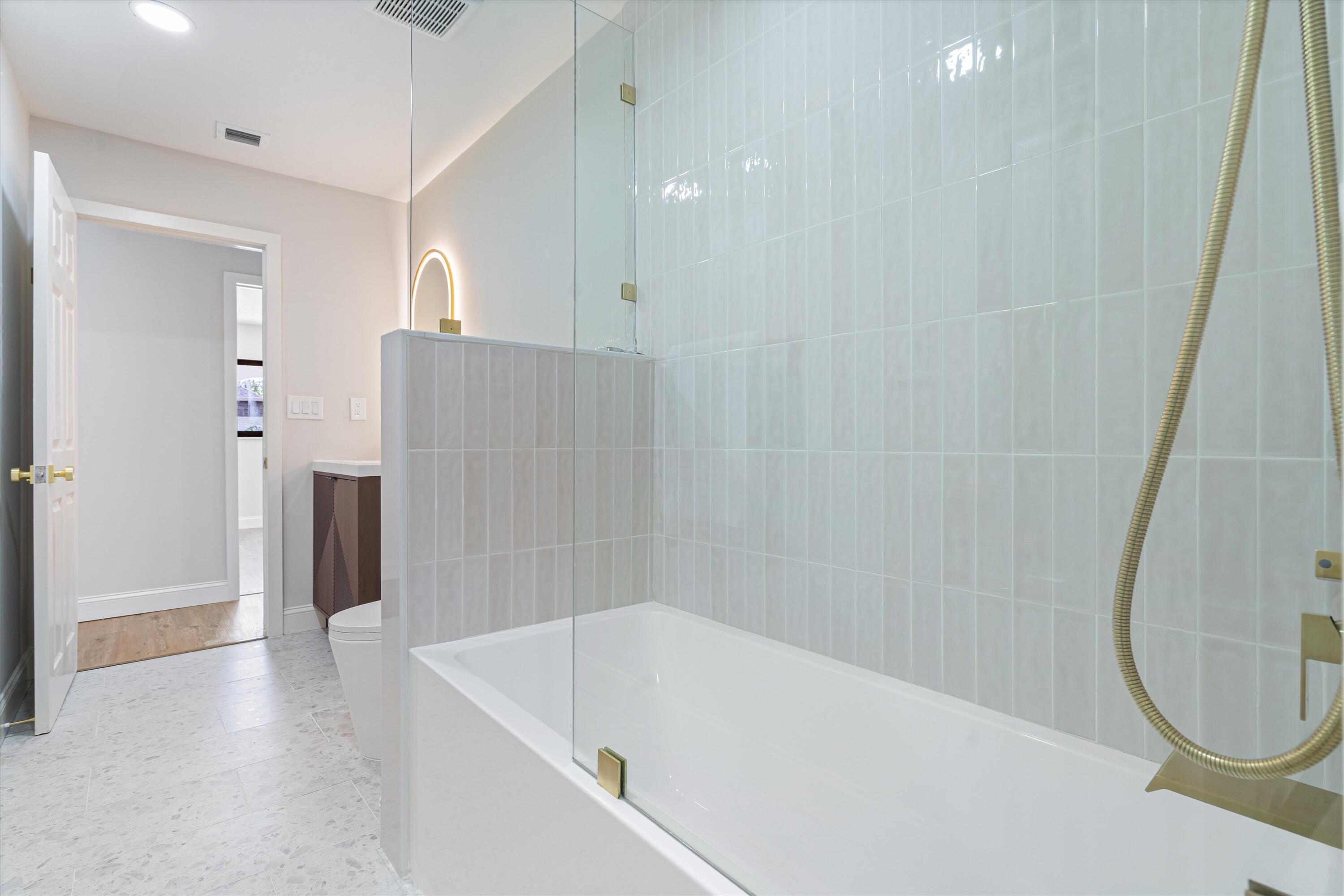 Bathroom featuring a glass-enclosed soaking tub with vertical tile surround, gold-tone hardware, and a vanity cabinet