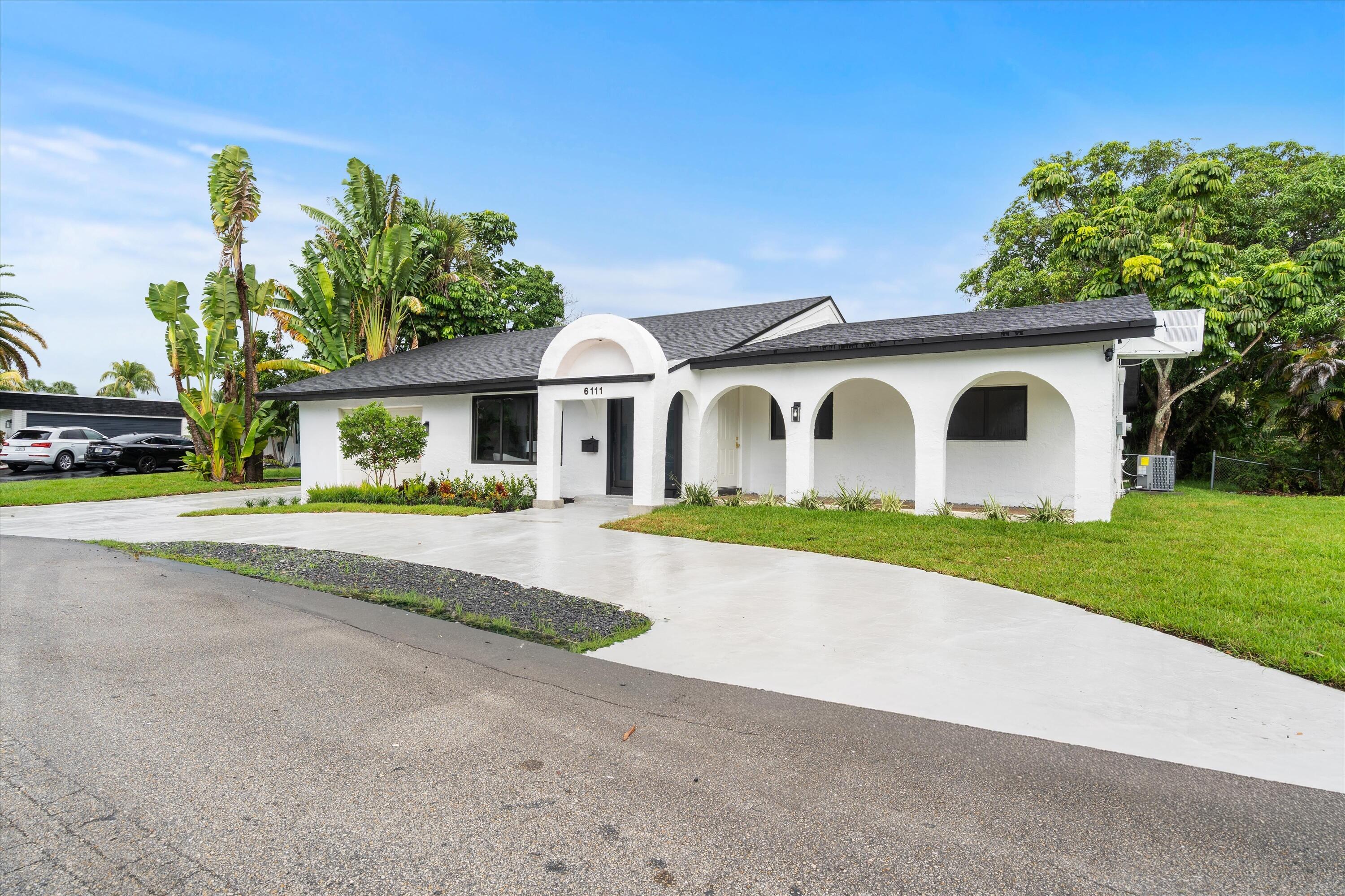 Single-story exterior featuring a white stucco facade, arched covered entryway, multi-arch colonnade, and a concrete driveway
