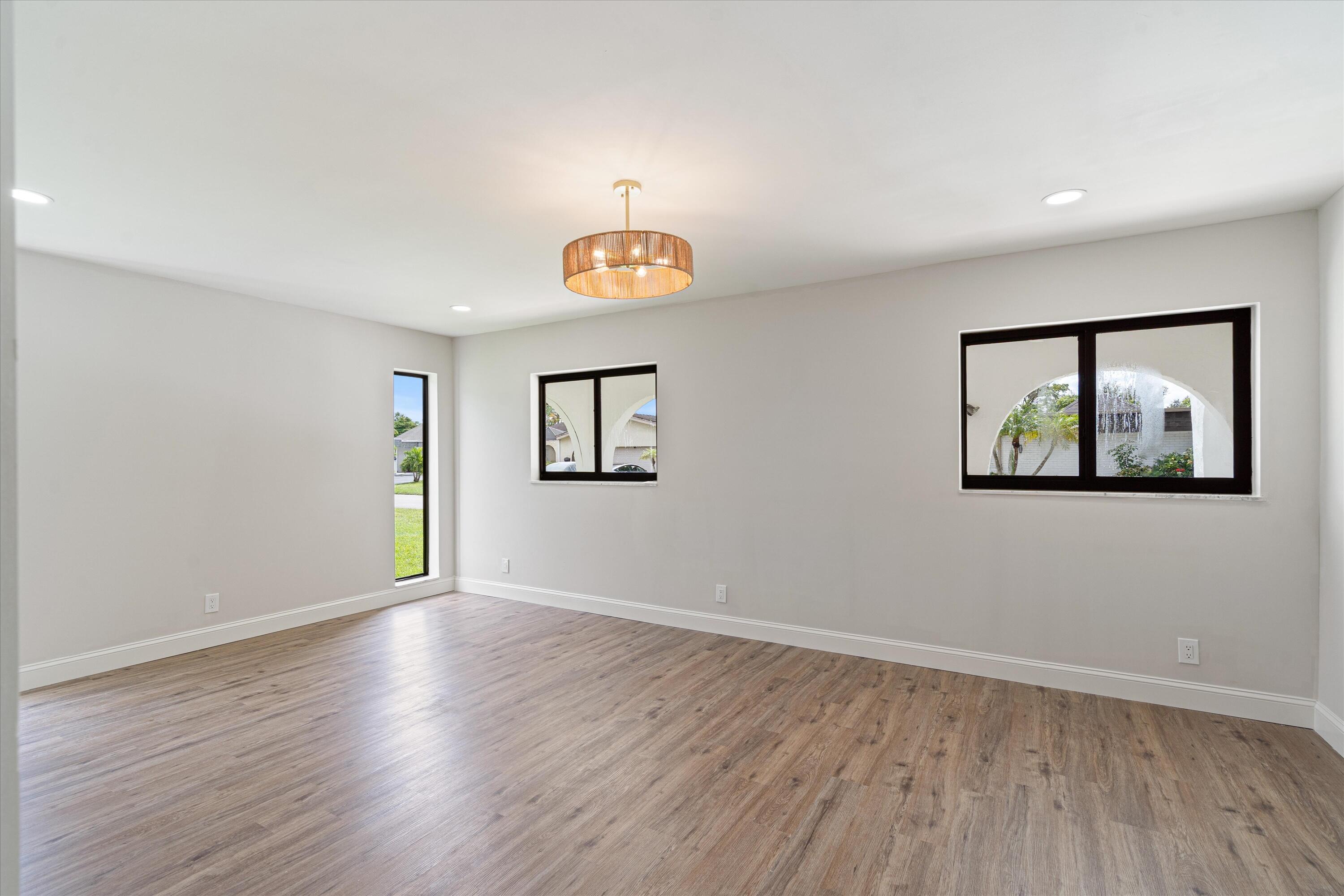 Neutral interior space featuring wood-finish flooring, recessed lighting, a drum chandelier, and black-framed windows