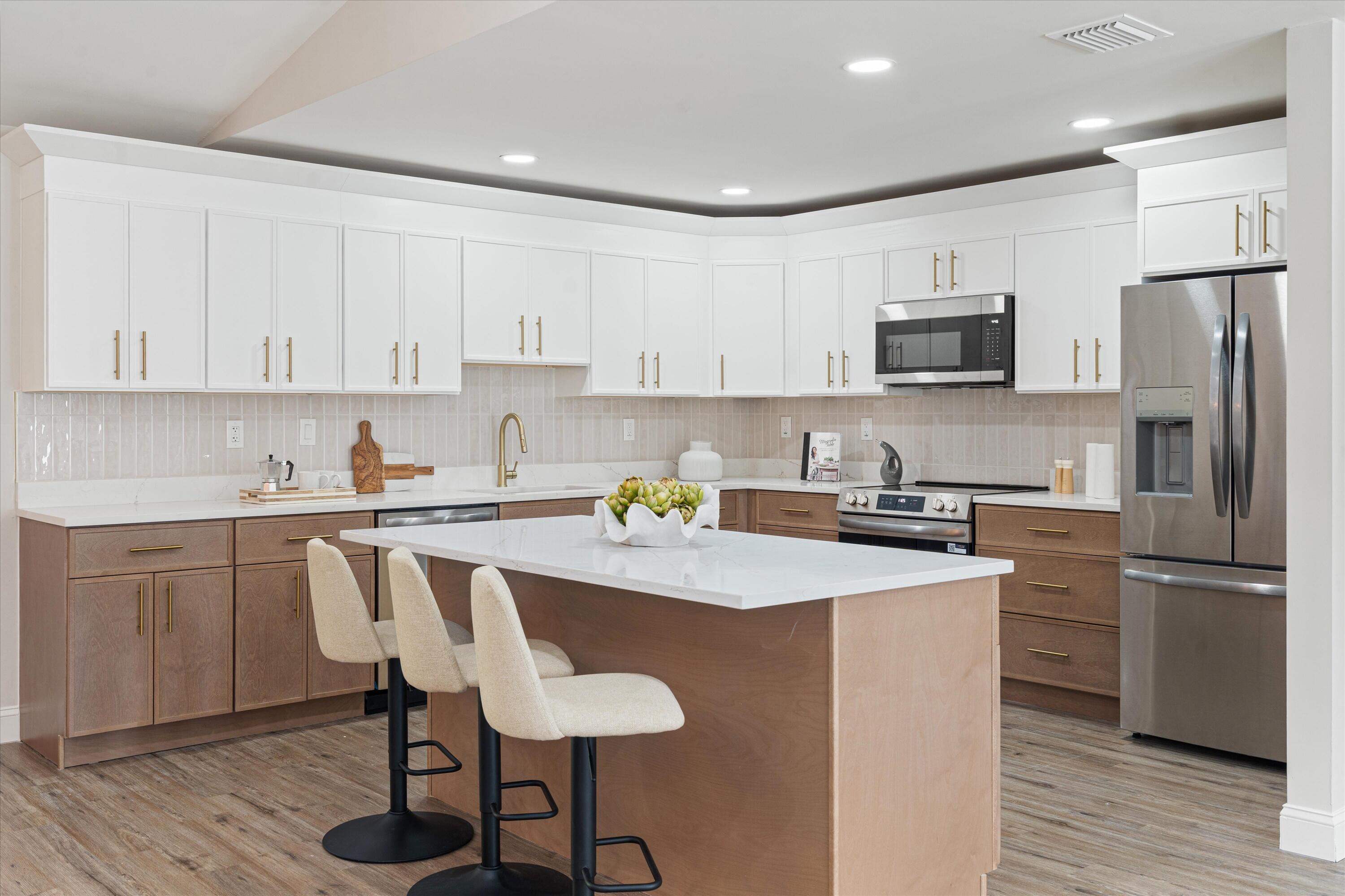 Kitchen featuring two-tone cabinetry, central island with seating space, stone-finish countertops, stainless steel appliances, and wood-finish flooring Kitchen featuring two-tone cabinetry, central island with seating space, stone-finish countertops, stainless steel appliances, and wood-finish flooring