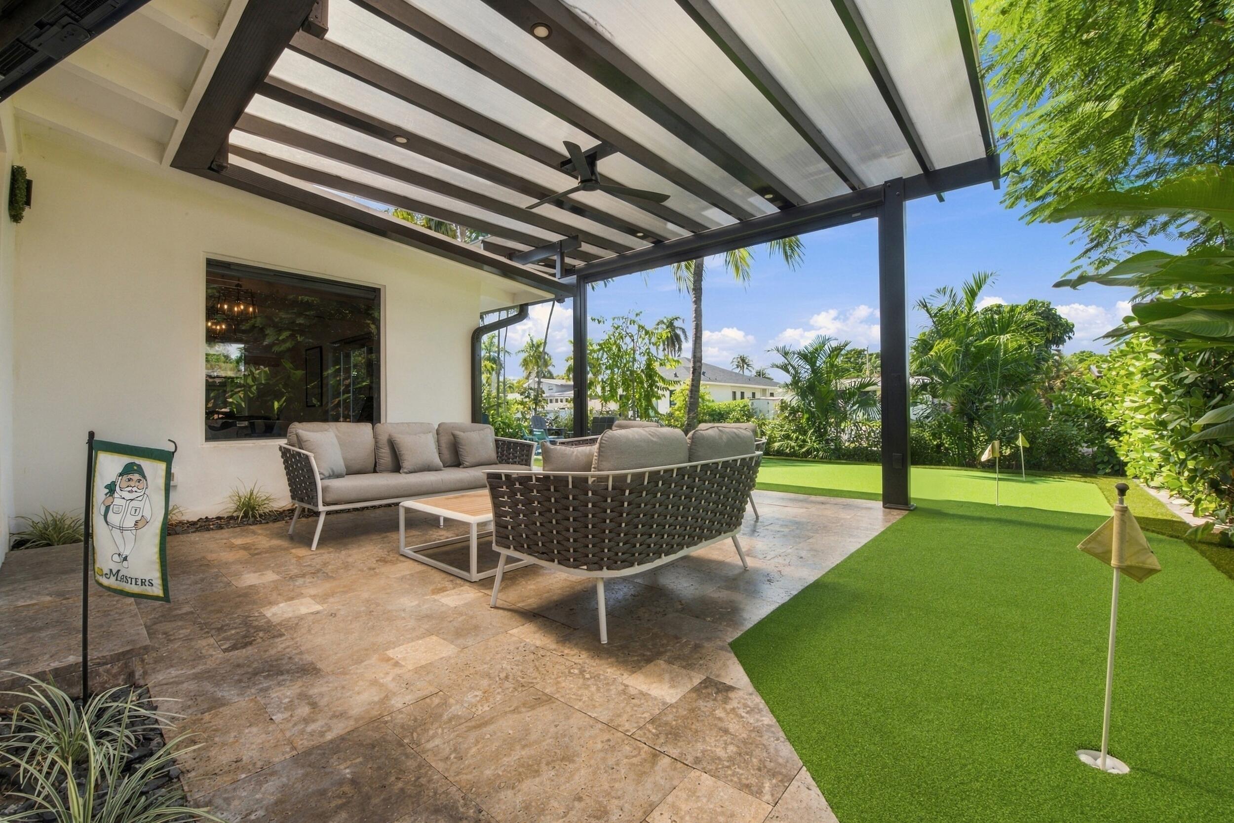 Covered patio with stone-tile flooring, metal pergola, integrated ceiling fan, and backyard putting green