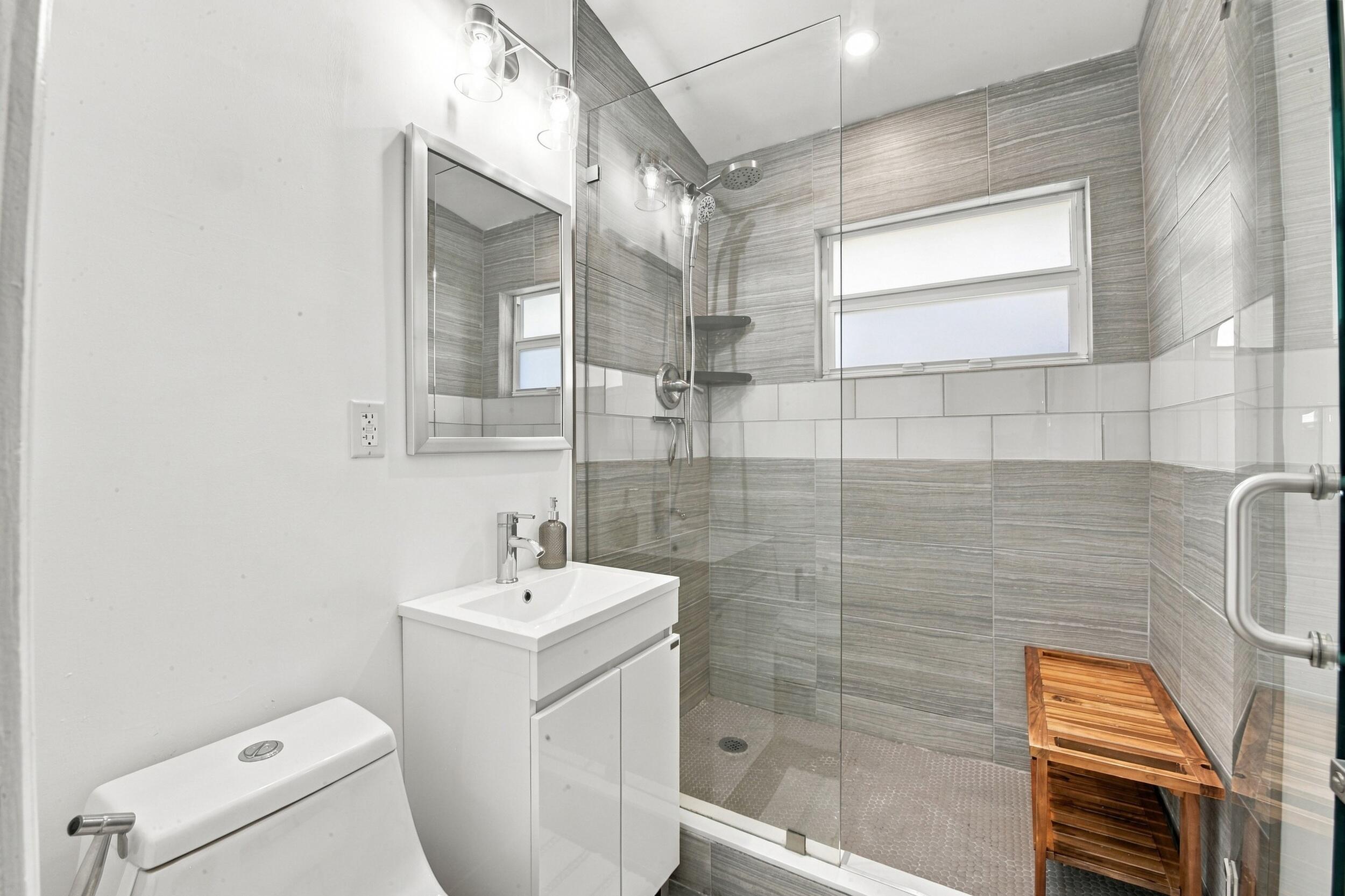 Bathroom featuring a glass-enclosed walk-in shower with horizontal tile surround, wall-mounted light fixtures, a vanity with an integrated basin, and an inset medicine cabinet