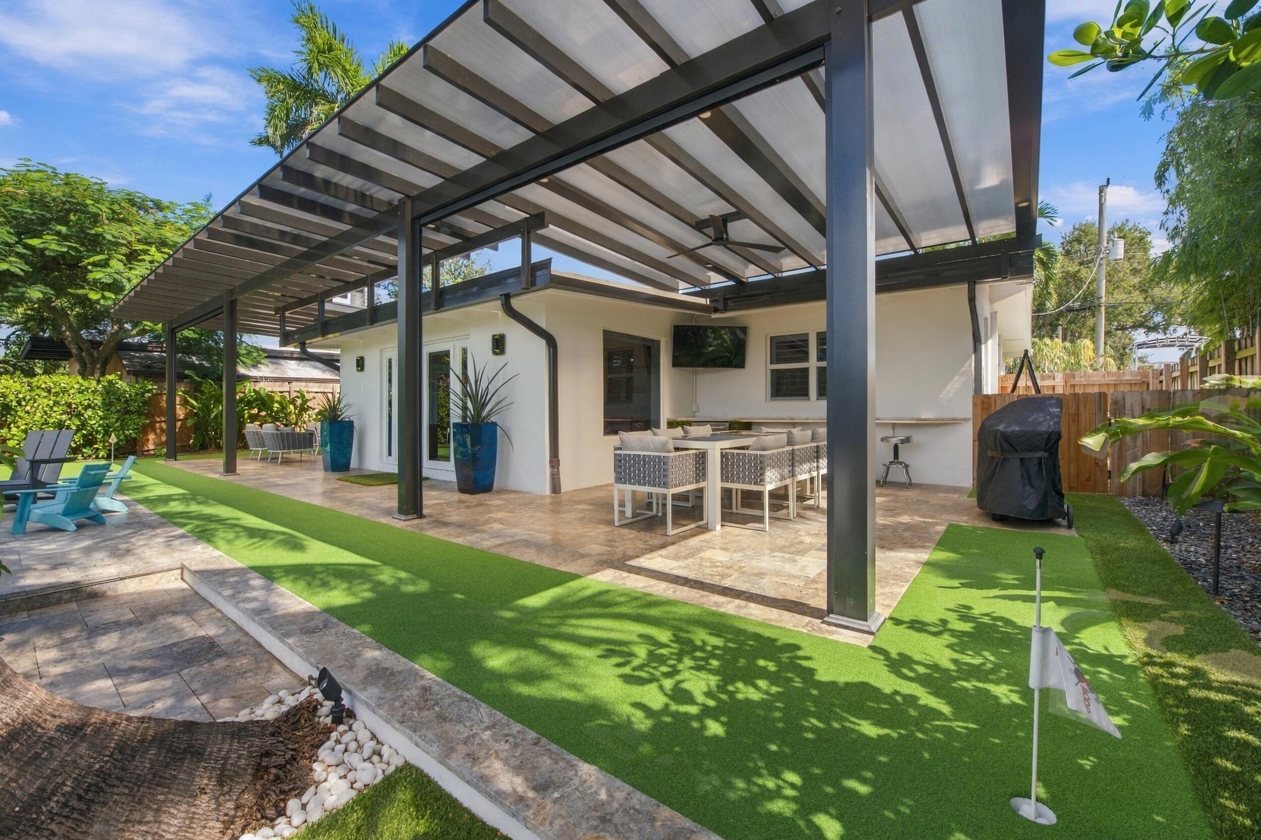 Covered outdoor patio featuring an overhead metal pergola, stone flooring, a built-in stone bar counter, and a putting green
