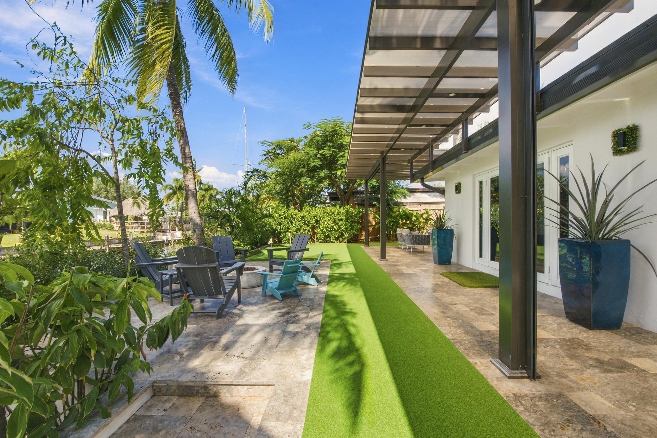 Covered patio featuring stone tile flooring and a metal-frame pergola, complemented by an outdoor area with stone hardscaping and a synthetic turf lawn