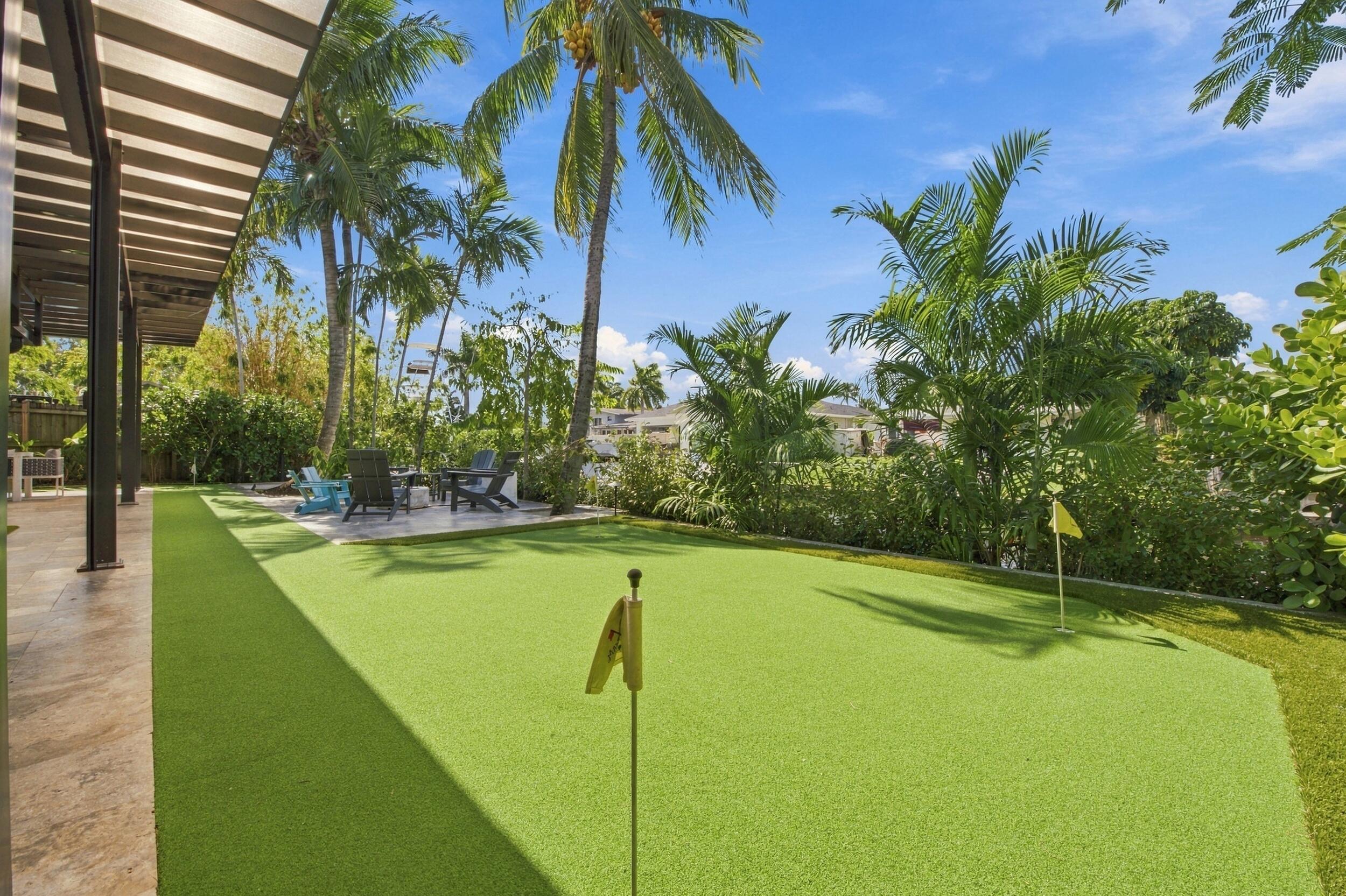 Backyard featuring a synthetic turf putting green, stone-tiled patio, covered veranda, and mature palm trees