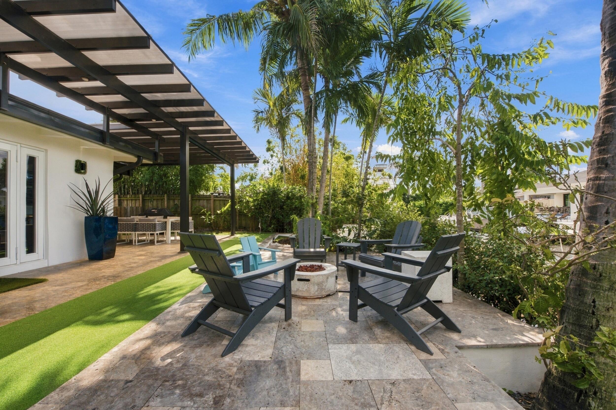 Patio area featuring natural stone pavers, a fixed metal-framed trellis, an integrated fire feature, and synthetic lawn accents