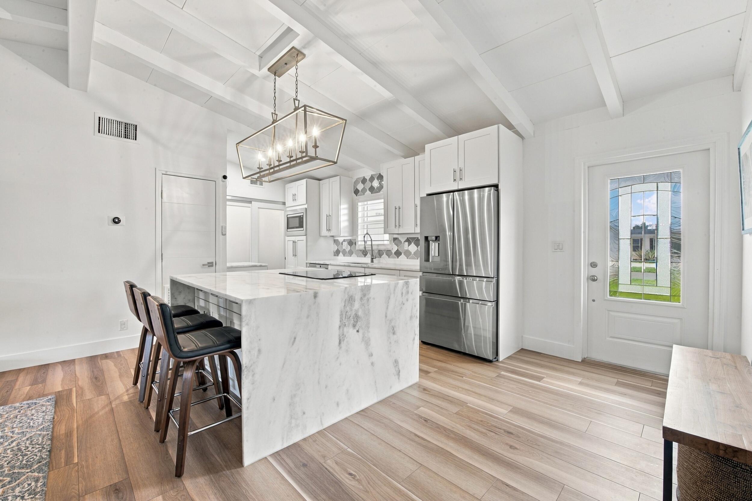 Kitchen featuring a waterfall-edge center island, wood-finish flooring, white shaker-style cabinetry, exposed ceiling beams, and a geometric tile backsplash