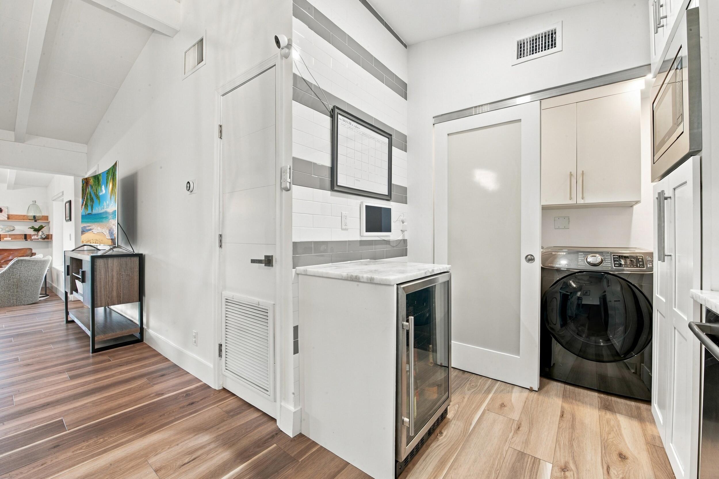 Utility space featuring wood-finish flooring, a built-in wine refrigerator with a stone countertop, a tiled accent wall, and a sliding door with a glass panel
