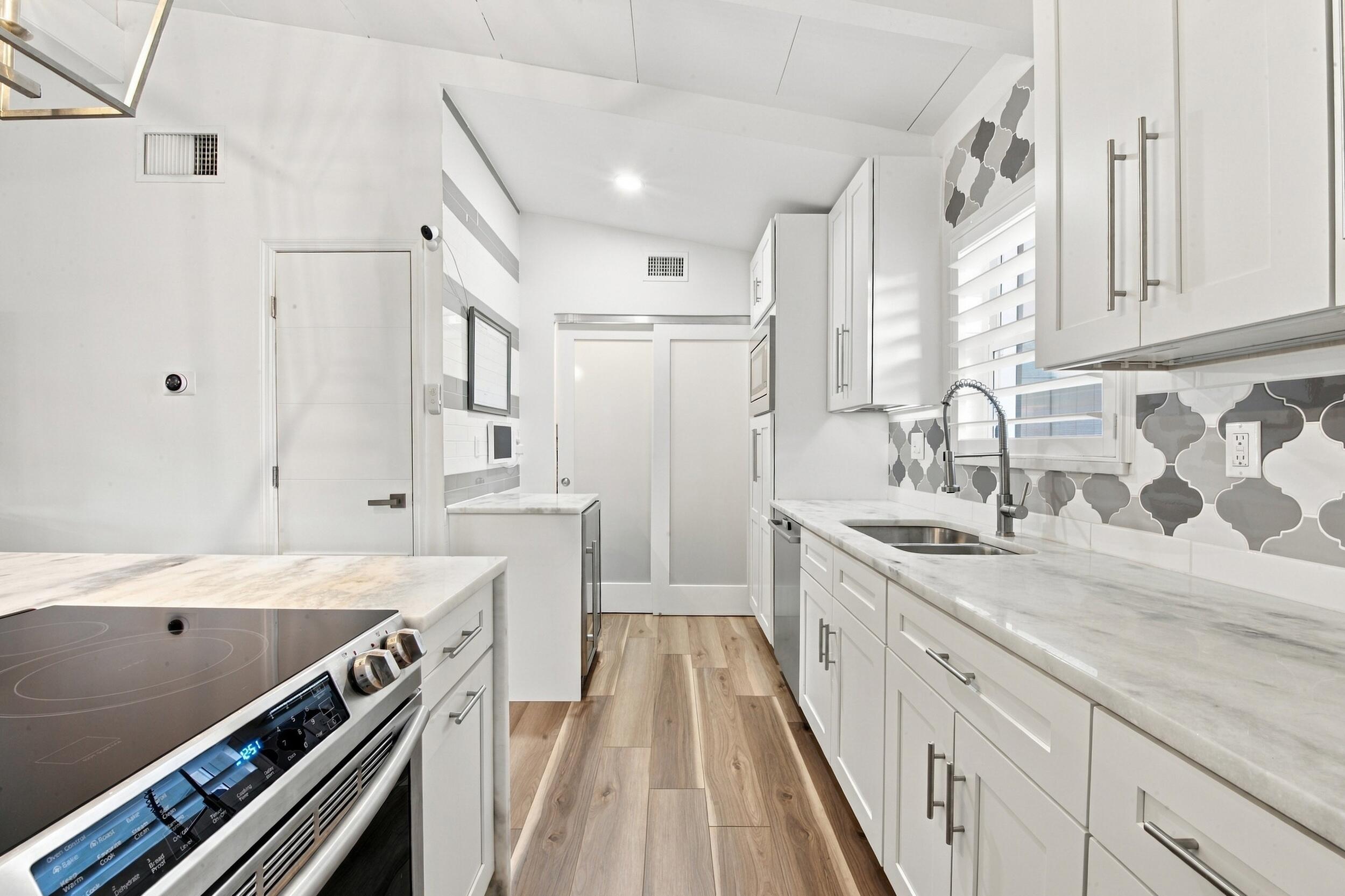 Kitchen featuring white cabinetry, stone-finish countertops, geometric tile backsplash, wood-finish flooring, and frosted glass sliding doors