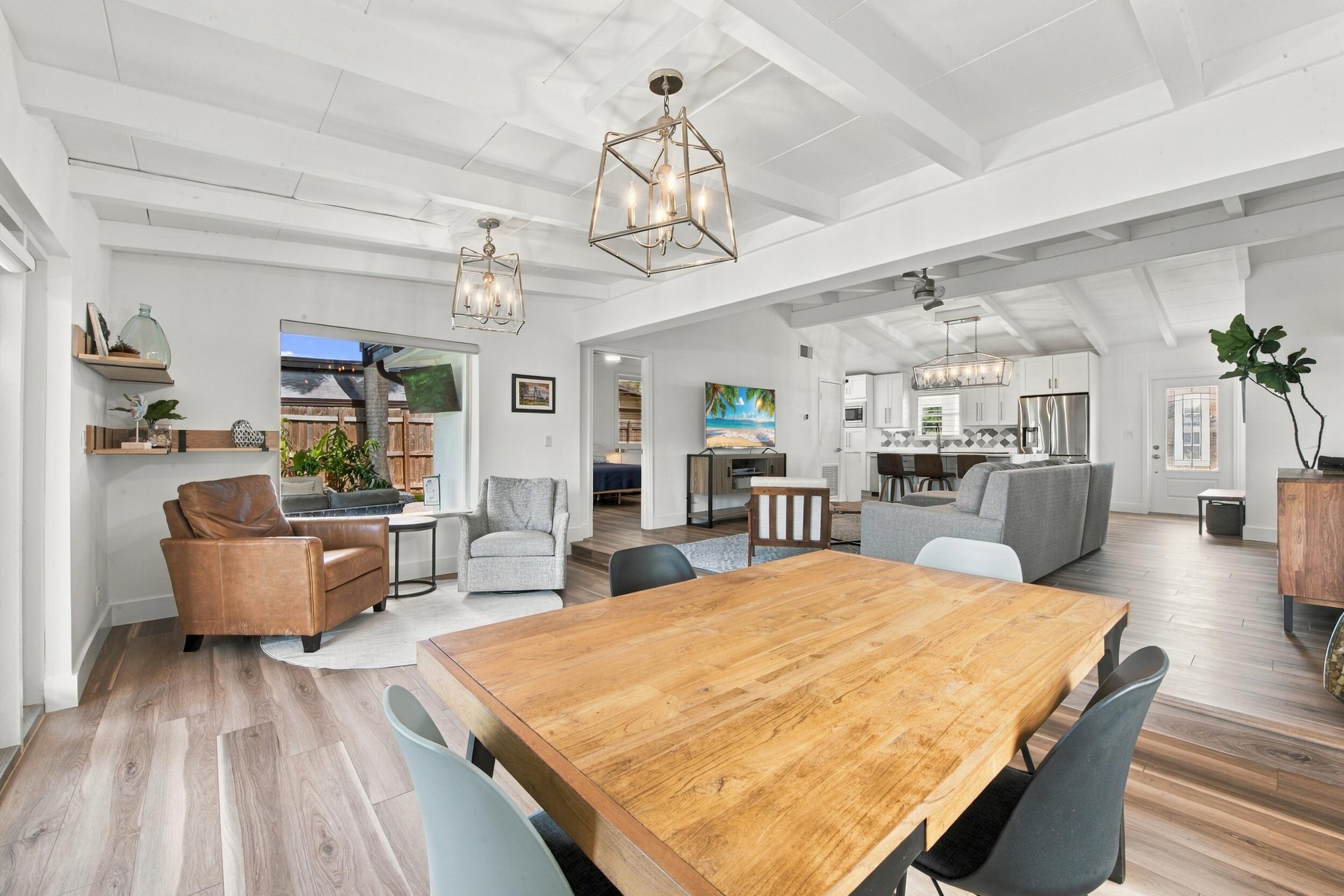 Open-concept interior featuring wood-finish flooring, exposed ceiling beams, custom wall-mounted shelving, and geometric lantern-style light fixtures