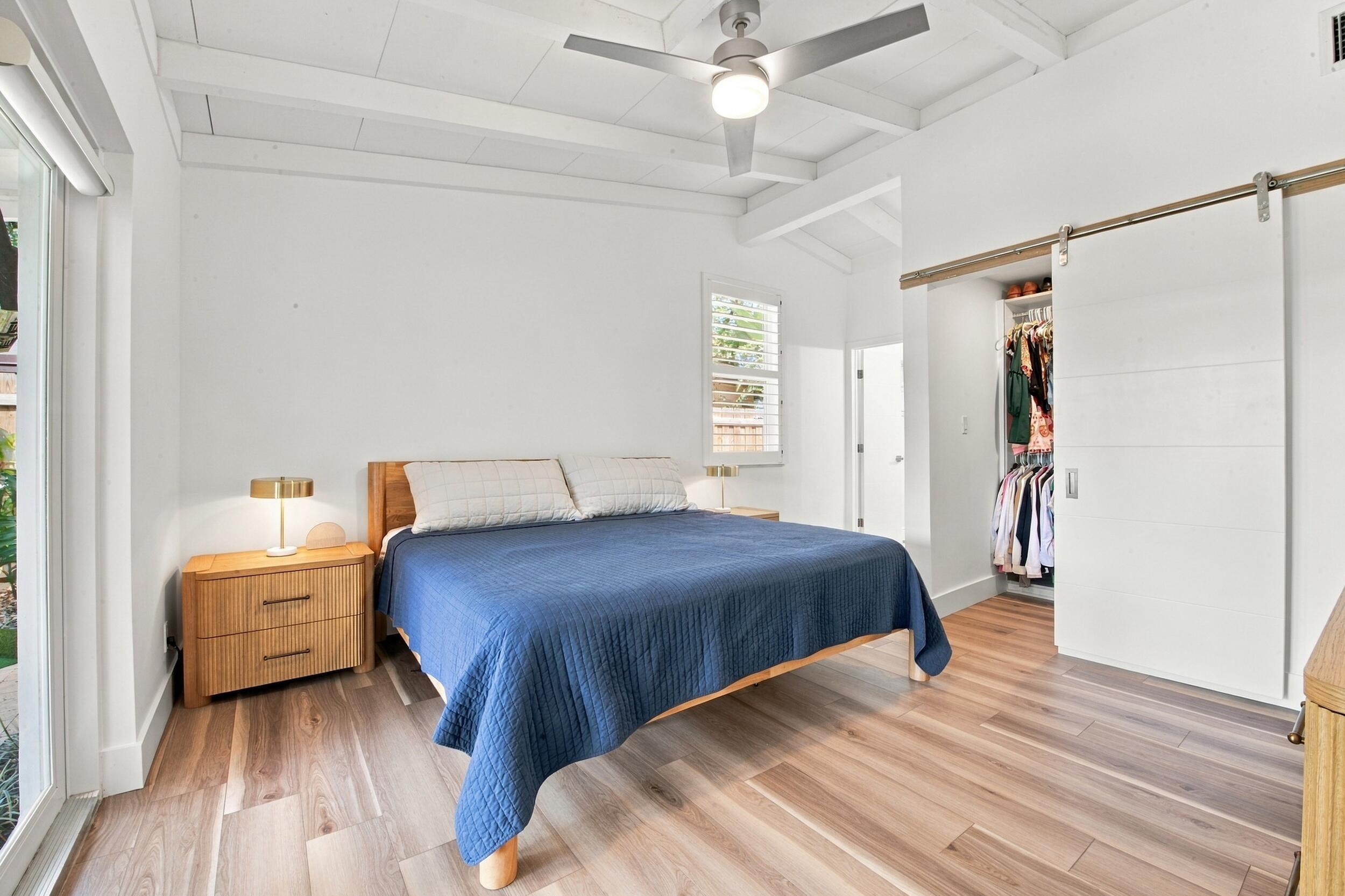 Wood-finish flooring, vaulted ceilings with exposed beams, sliding barn-style closet door, ceiling fan with integrated lighting, and plantation shutters