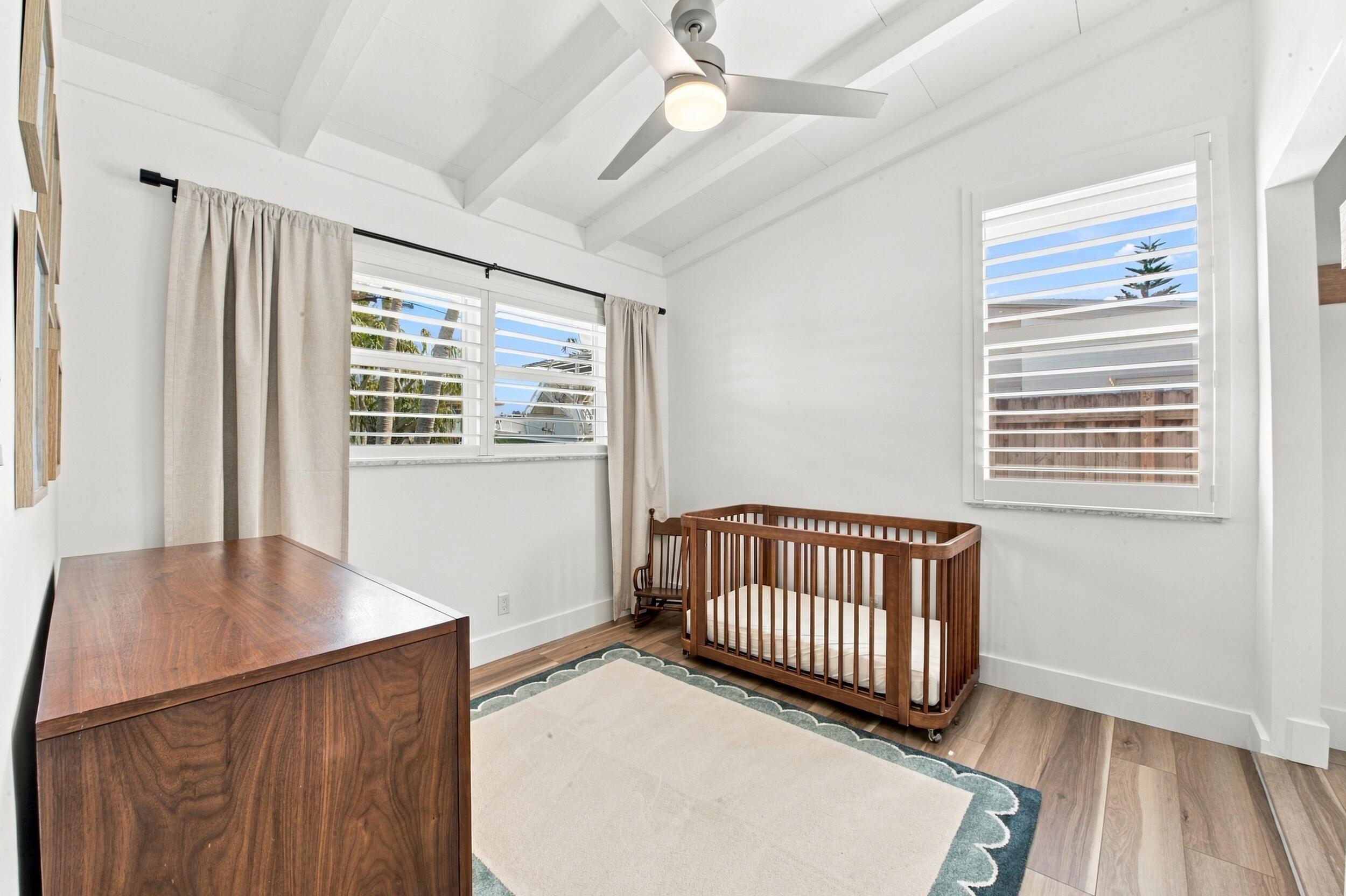 Wood-finish flooring, vaulted ceilings with exposed beams, three windows with plantation shutters, and a modern ceiling fan with integrated lighting