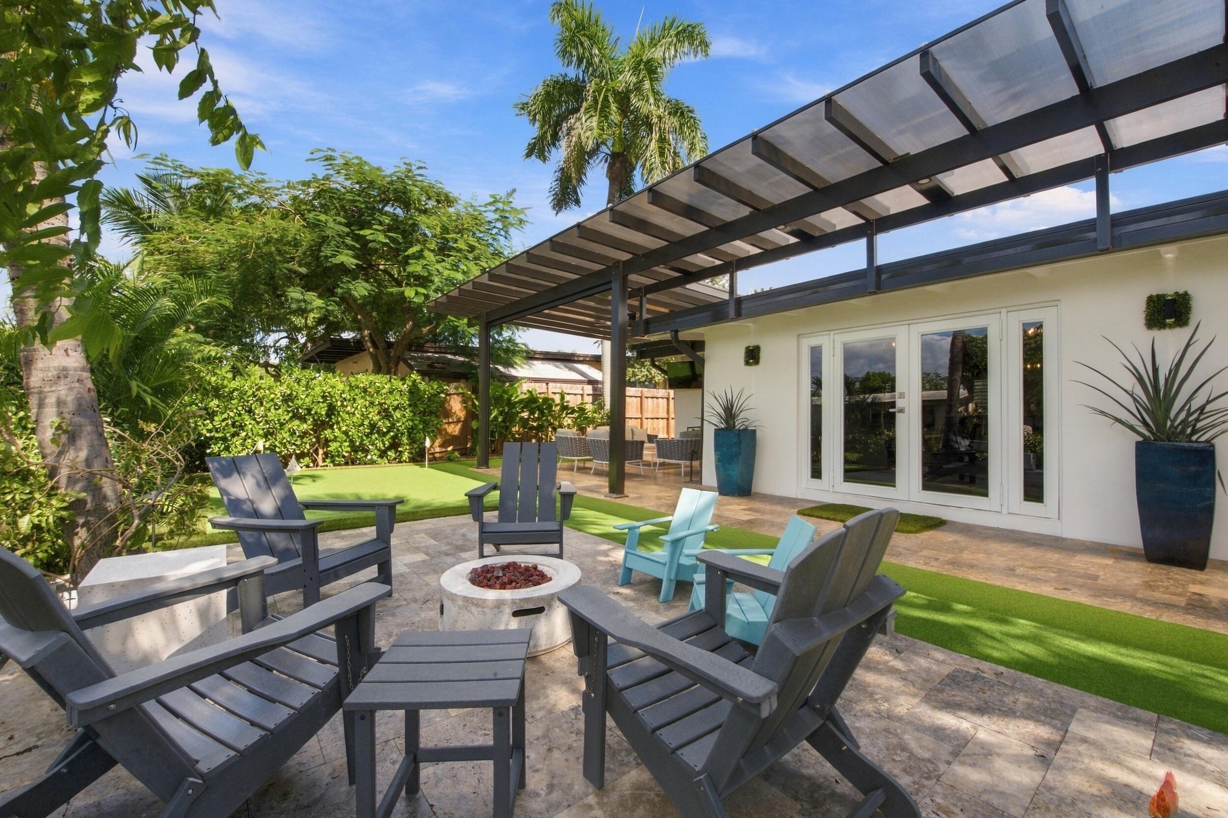 Outdoor patio featuring stone tile flooring, a metal-framed overhead trellis, synthetic turf accents, and white French doors