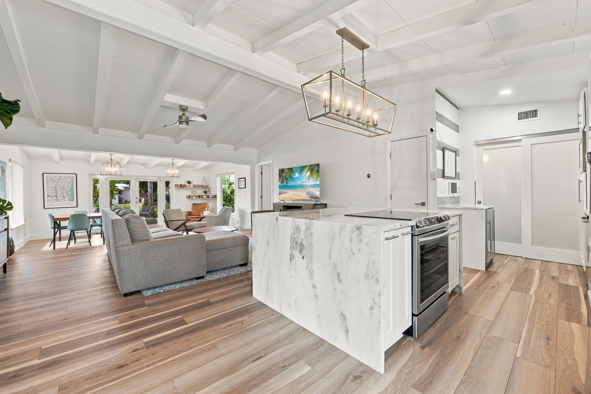 Kitchen island with stone-finish waterfall countertop, wood-finish flooring, exposed beam vaulted ceiling, and rectangular metal frame pendant lighting