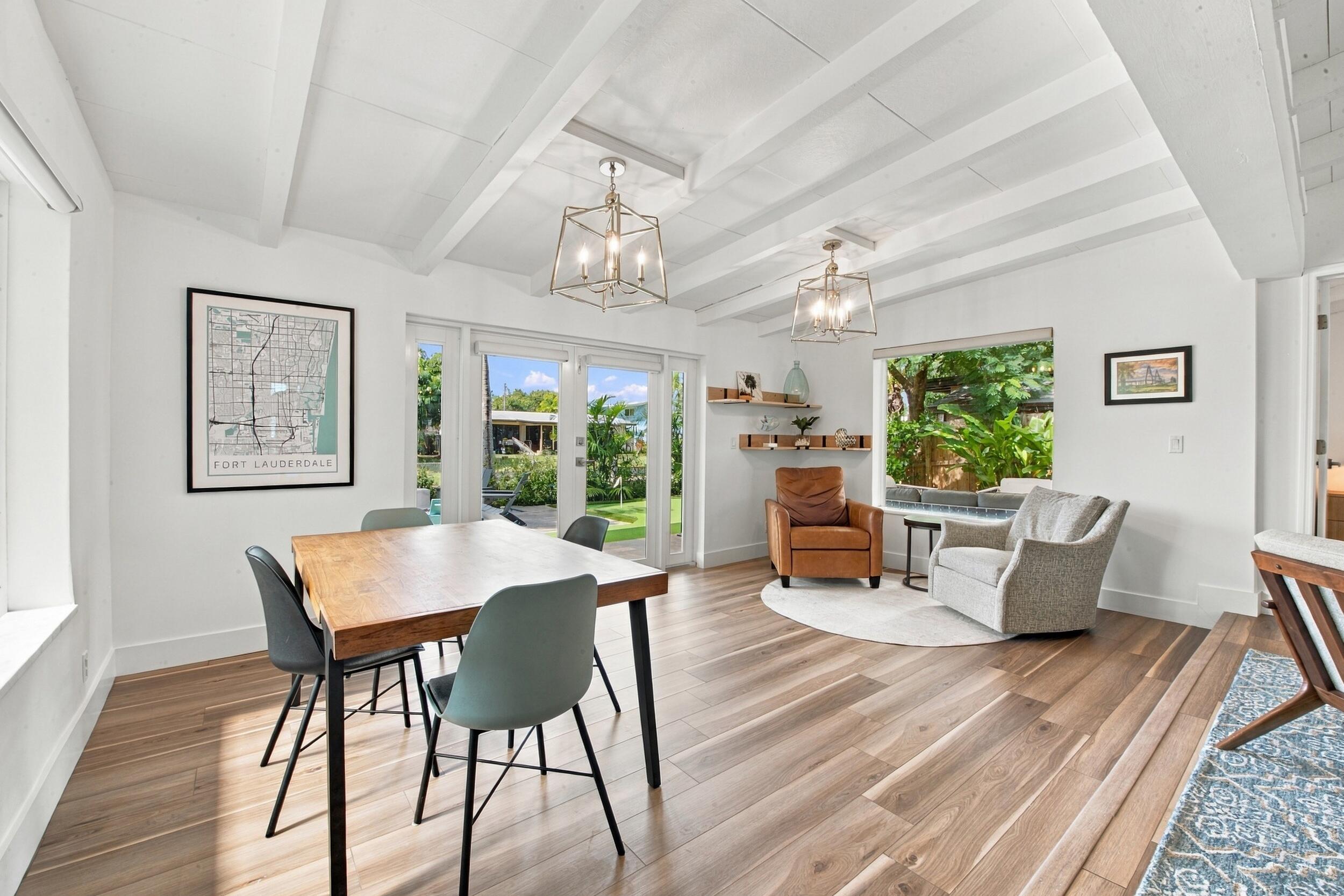 Exposed beam vaulted ceiling, wood-finish flooring, dual geometric metal chandeliers, glass-paneled double doors, and built-in floating wall shelving