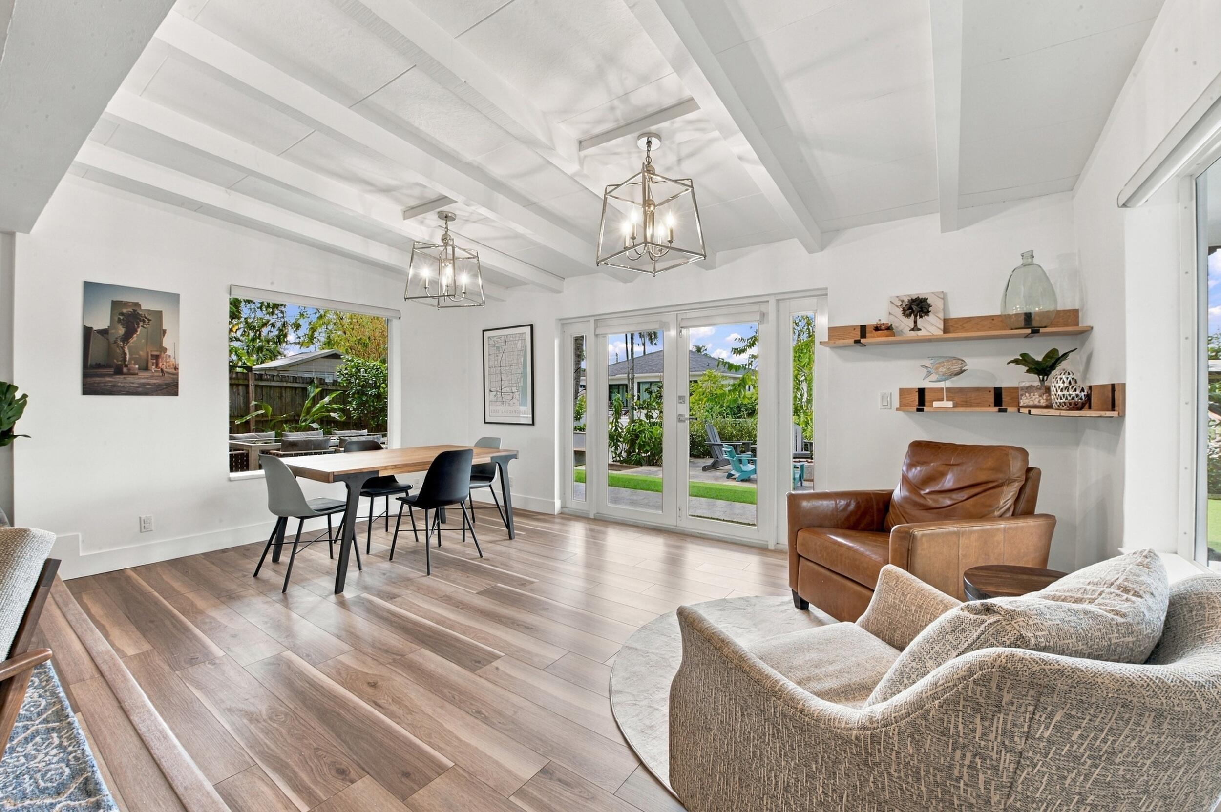 Vaulted ceilings with exposed beams, wood-finish flooring, two metal lantern-style pendant fixtures, glass-paned double doors, and built-in floating wall shelving