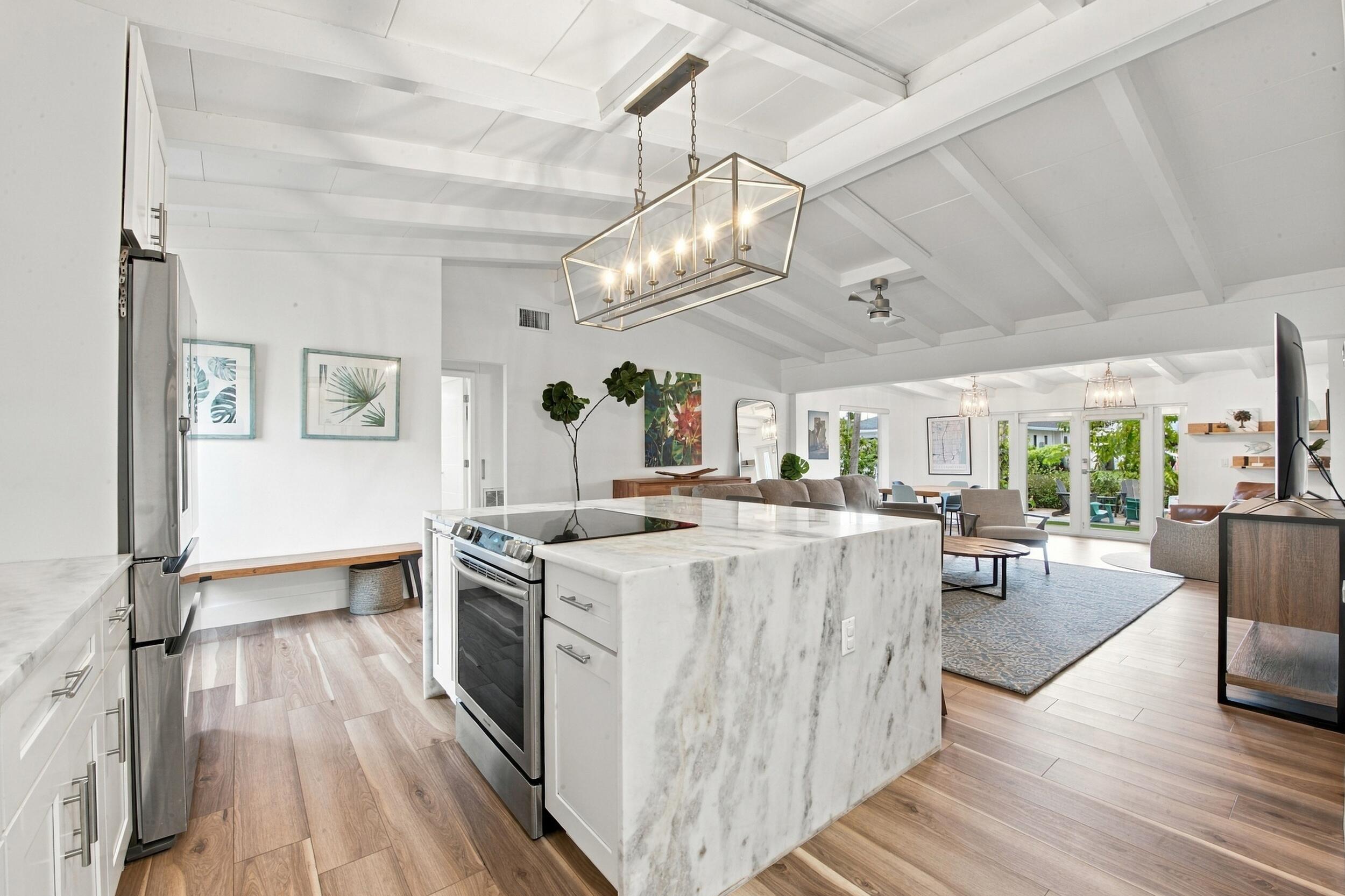 Kitchen featuring a stone-topped waterfall island, stainless steel range, wood-finish flooring, vaulted ceilings with exposed beams, and a geometric linear pendant light