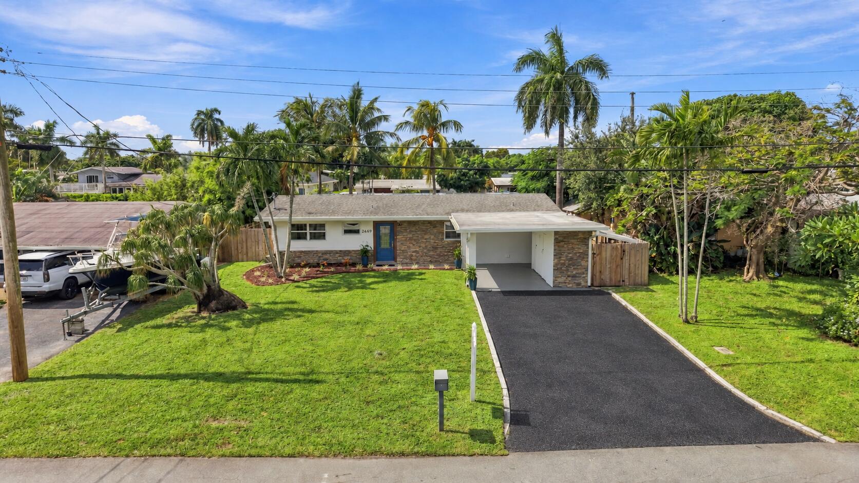 Single-story exterior featuring stone veneer facade, paved driveway, attached carport, and manicured landscaping