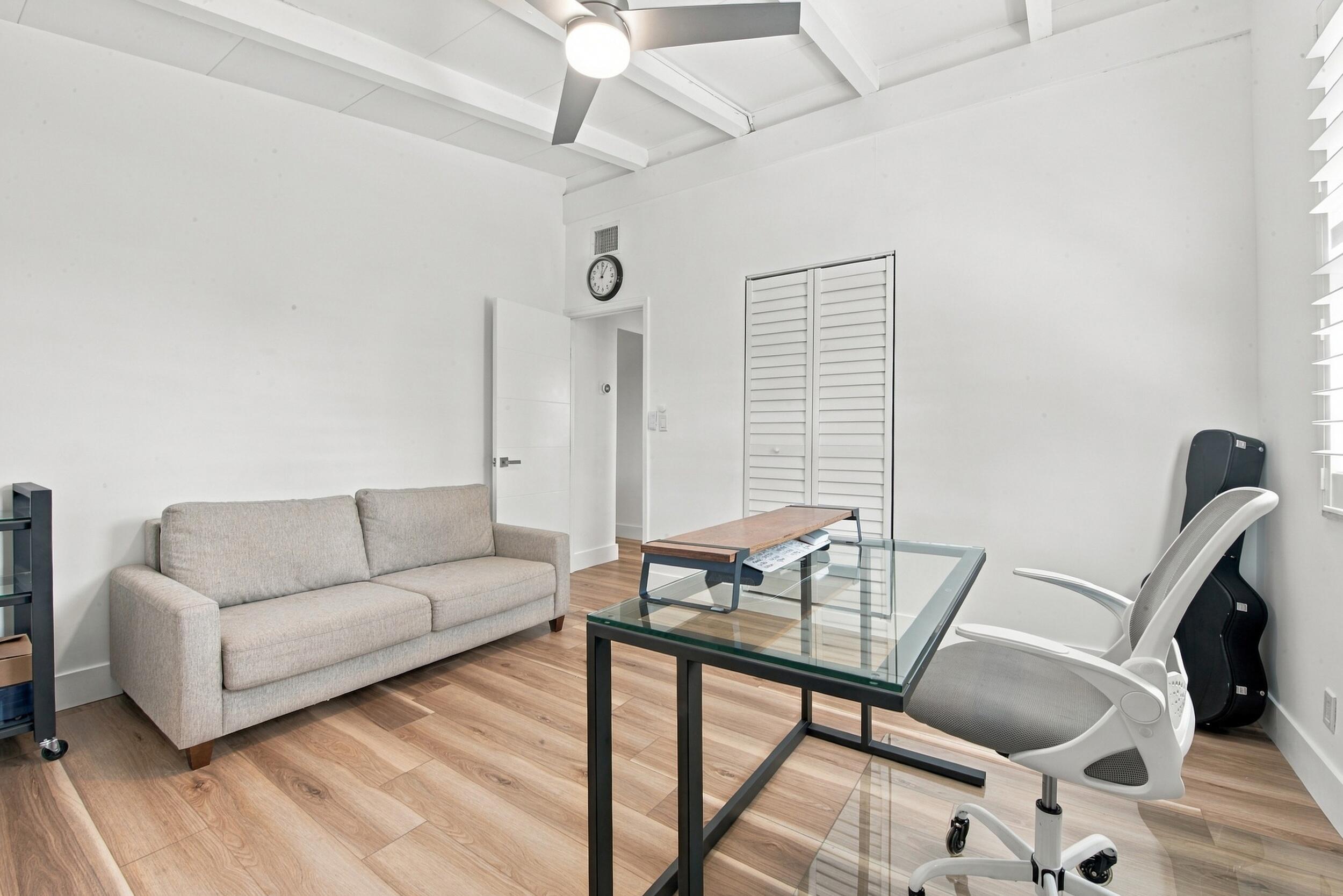 Room featuring wood-finish flooring, exposed ceiling beams, a ceiling fan, and louvered-panel closet doors