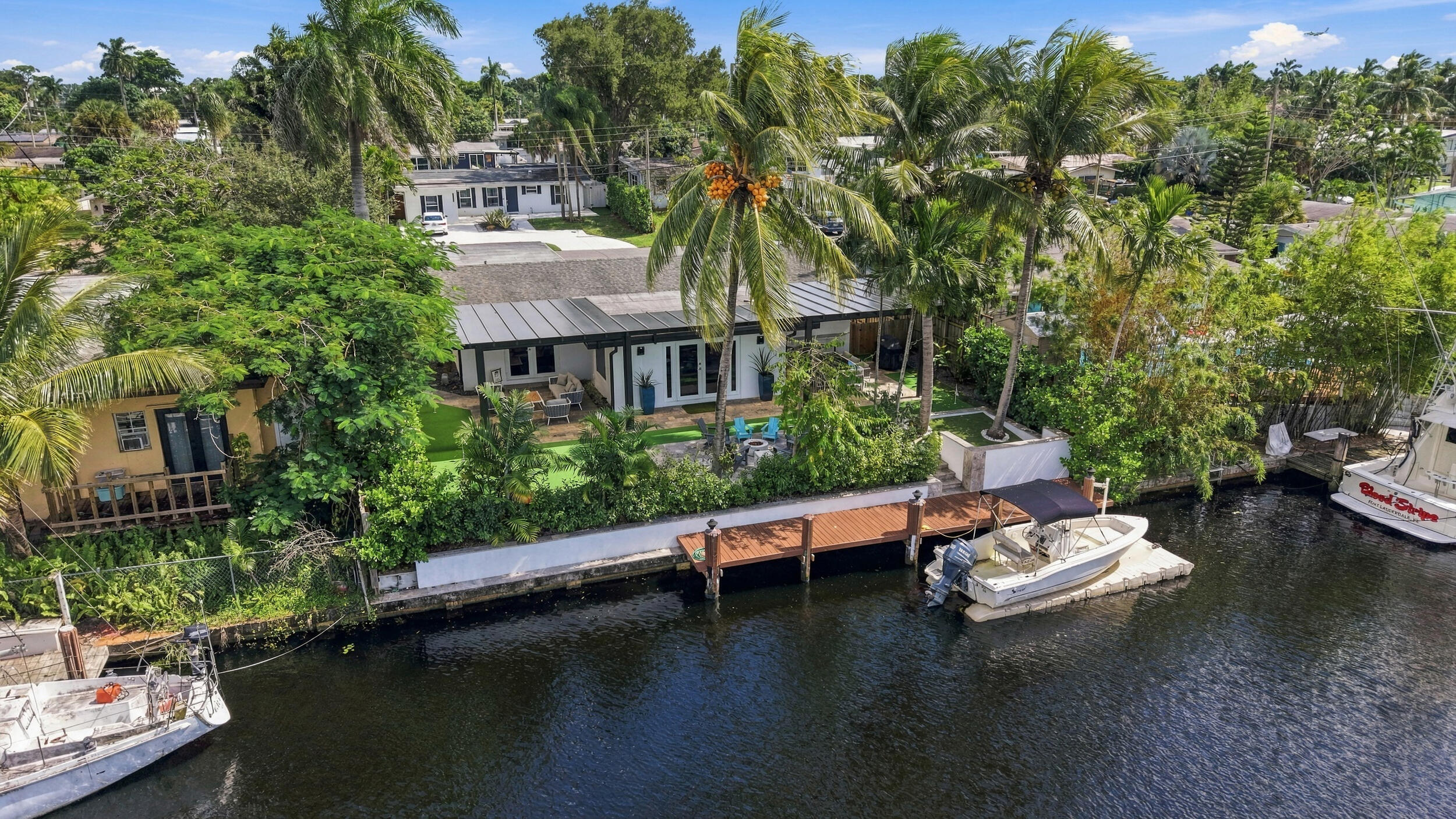 Waterfront property featuring a private wooden dock, a metal-seam roof, mature palm trees, and a concrete bulkhead