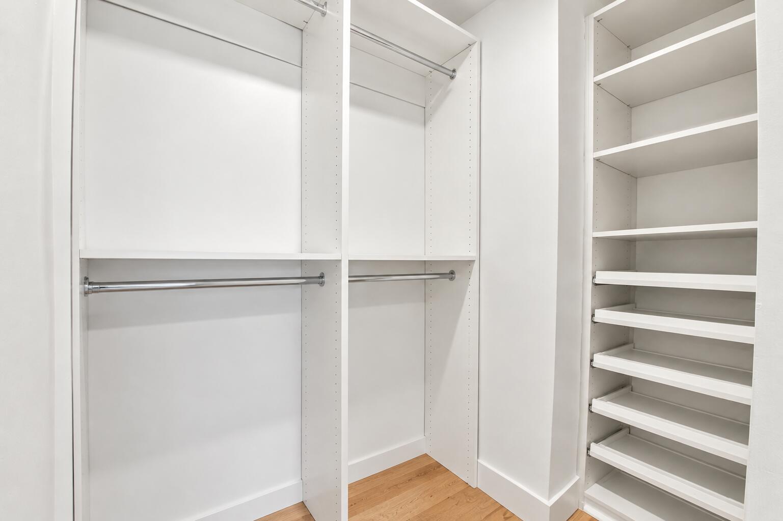 Custom closet system featuring white shelving, multiple hanging rods, and integrated pull-out drawers over wood-finish flooring