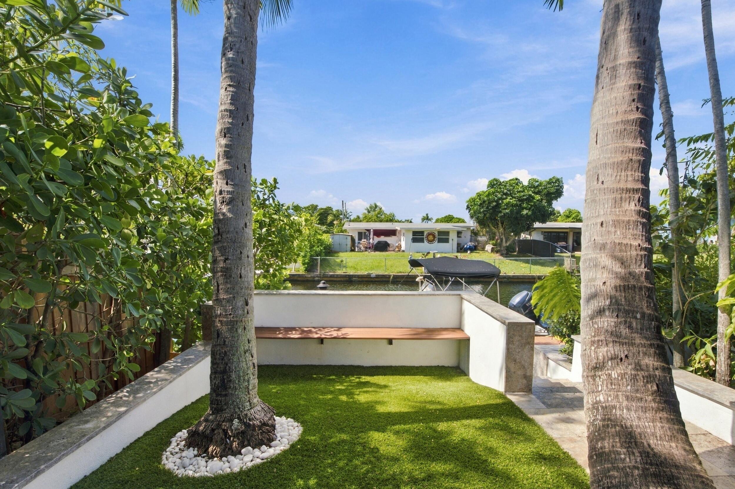 Waterfront outdoor space featuring a stone-capped perimeter wall, integrated wood-finish bench seating, synthetic turf ground cover, and mature palm trees