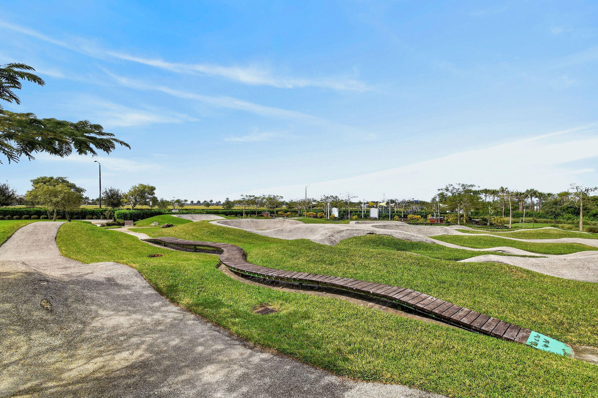 Pumptrack featuring varied terrain, a wooden ramp, and surrounding green spaces
