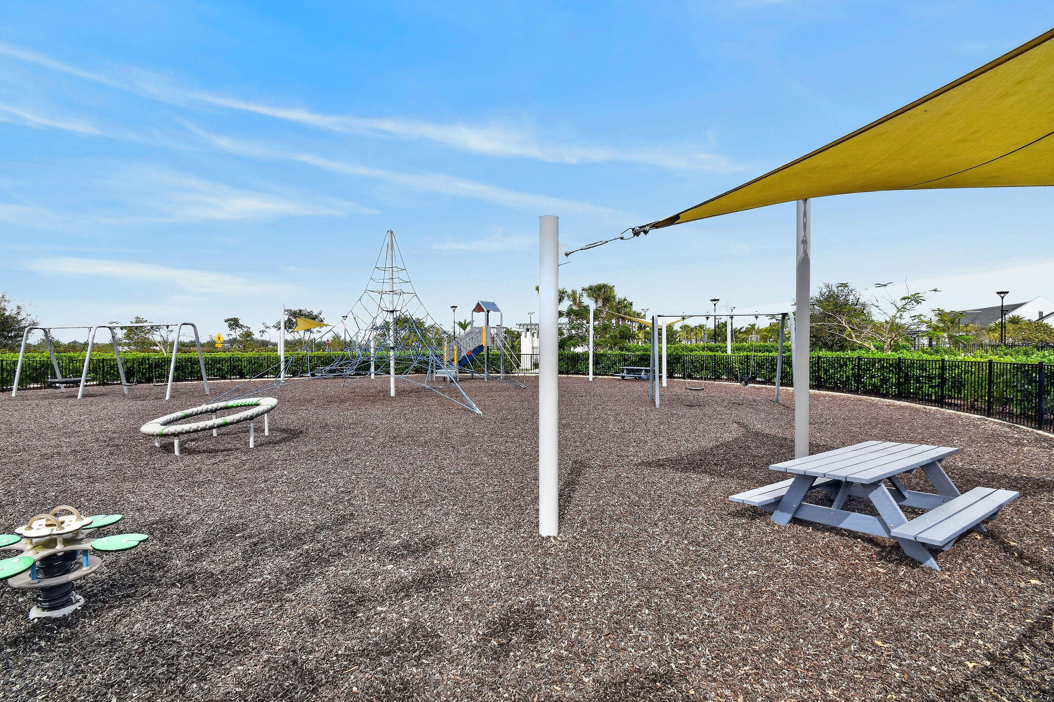 Community playground featuring diverse equipment, a shaded picnic area, and a protective ground surface
