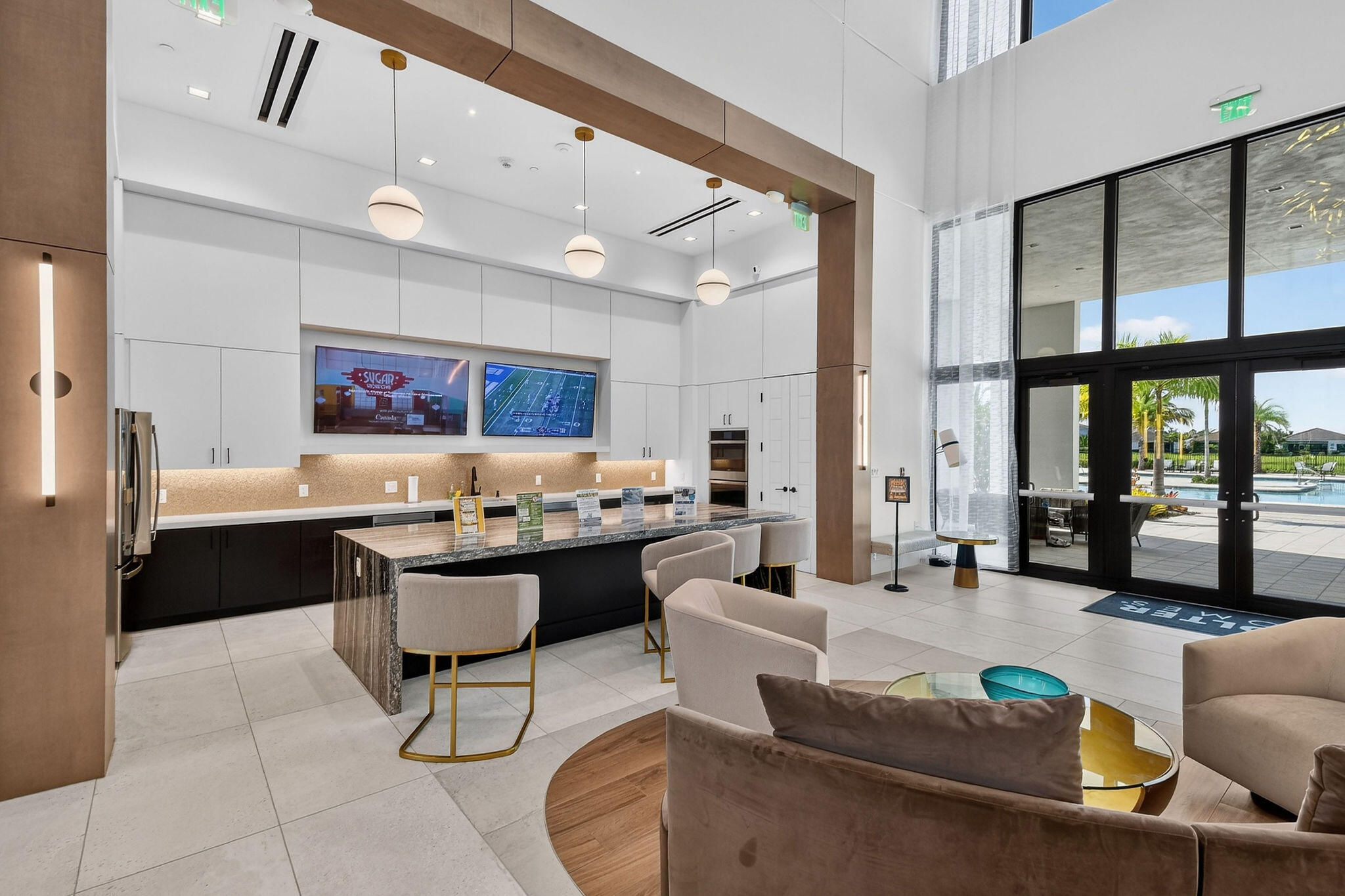 Spacious common area featuring an expansive counter with integrated seating, dual wall-mounted displays, and floor-to-ceiling windows