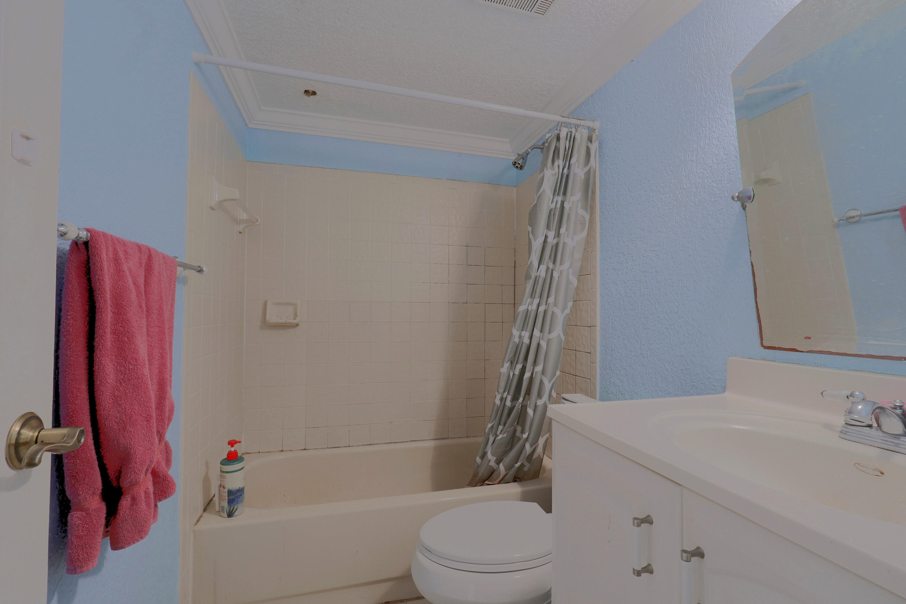 Bathroom featuring a tub-shower combination with tile surround, white vanity cabinet with a molded sink, and a wall-mounted mirror Bathroom featuring a tub-shower combination with tile surround, white vanity cabinet with a molded sink, and a wall-mounted mirror