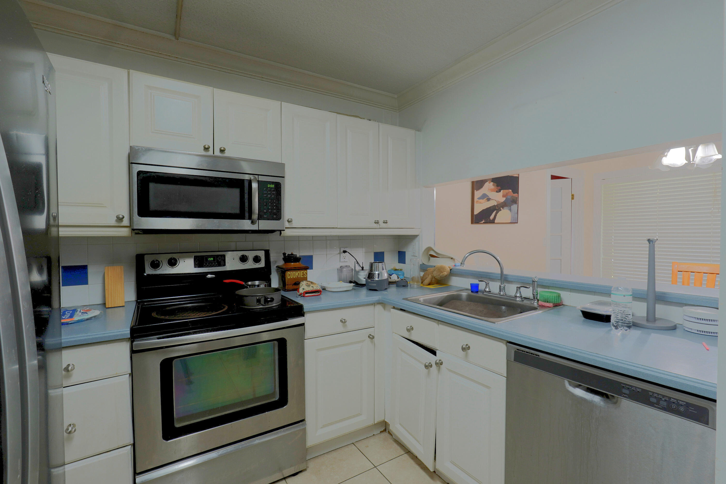 Kitchen featuring white shaker-style cabinetry, stainless steel appliances, solid-surface countertops, and a stainless steel sink with a goose-neck faucet Kitchen featuring white shaker-style cabinetry, stainless steel appliances, solid-surface countertops, and a stainless steel sink with a goose-neck faucet