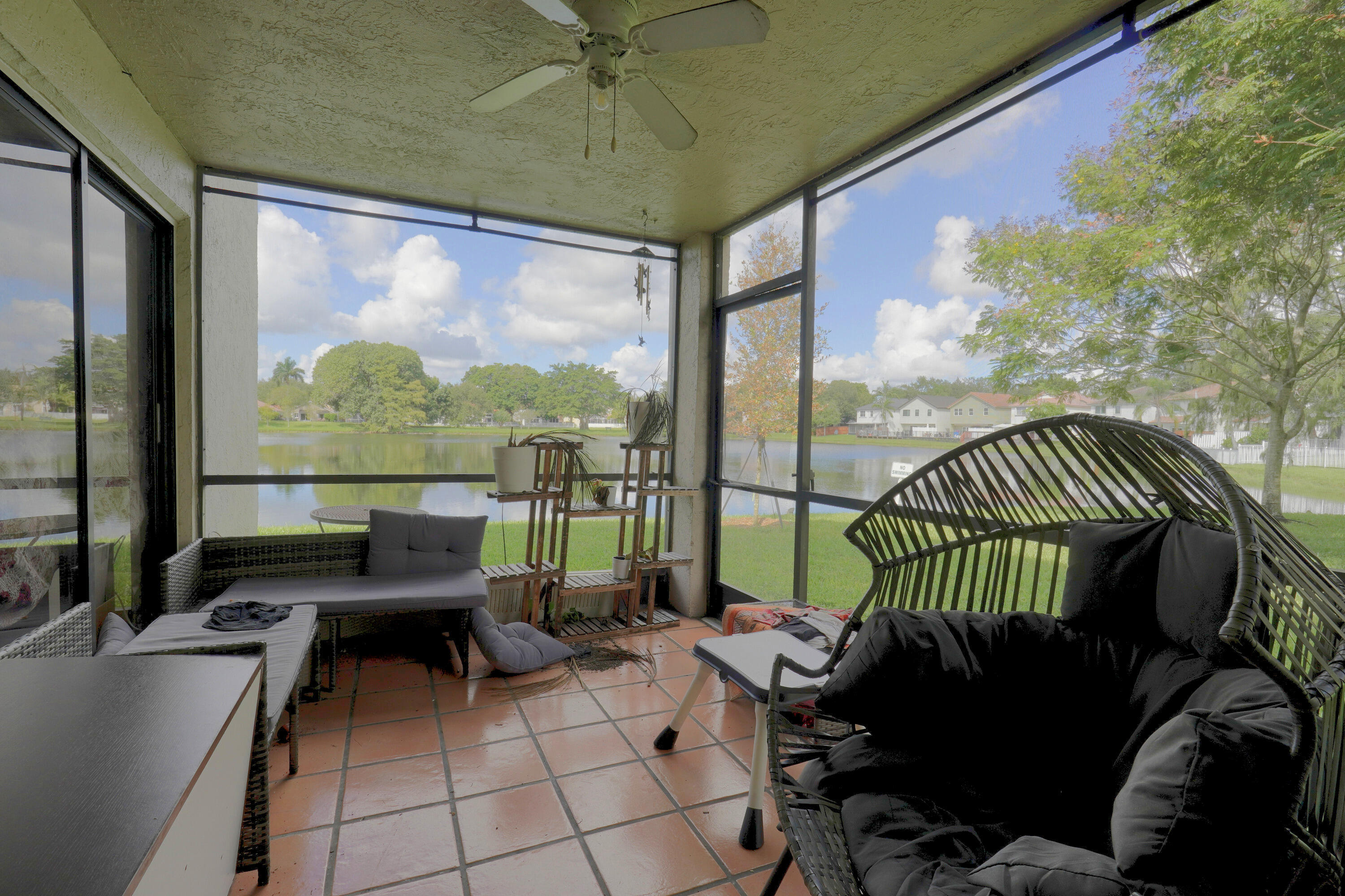 Screened lanai featuring tile flooring, a ceiling fan, and metal framing with full-height screens overlooking a lake Screened lanai featuring tile flooring, a ceiling fan, and metal framing with full-height screens overlooking a lake