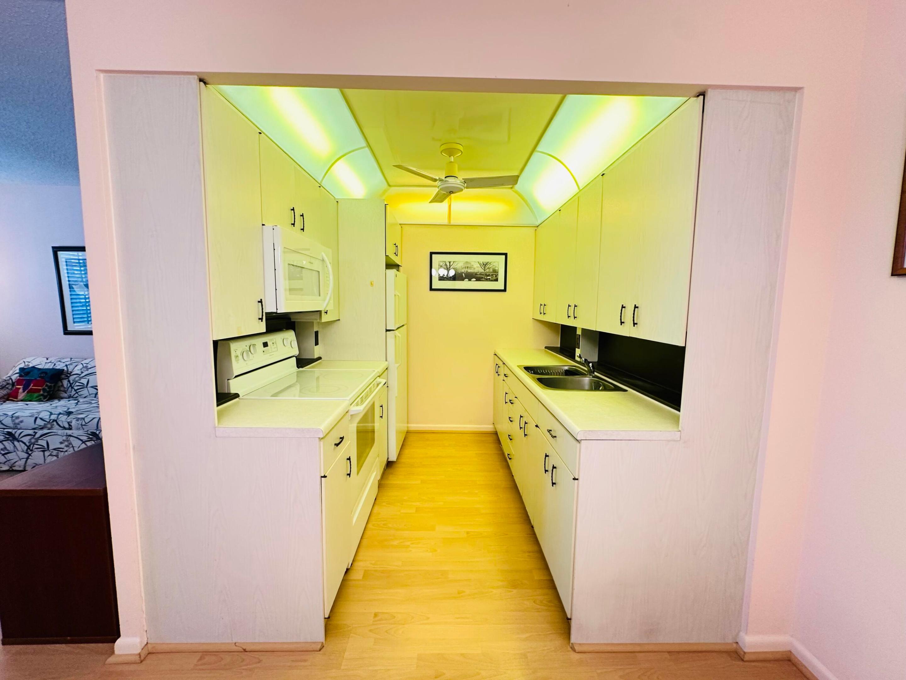 Galley kitchen featuring light-toned cabinetry, solid surface countertops, integrated recessed lighting, dual-basin sink, and laminate flooring Galley kitchen featuring light-toned cabinetry, solid surface countertops, integrated recessed lighting, dual-basin sink, and laminate flooring