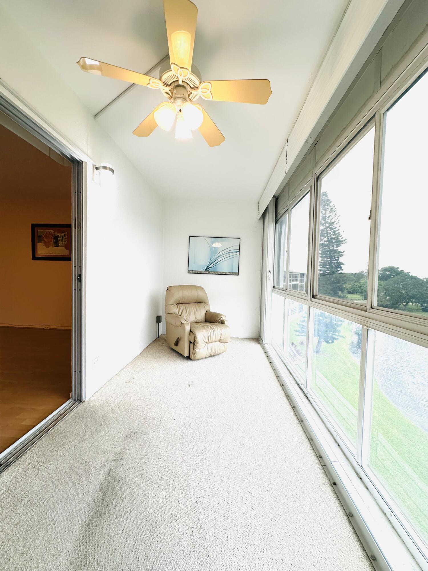 Enclosed porch featuring expansive multi-pane glass walls, carpeted flooring, and a ceiling-mounted light fixture with a three-blade fan