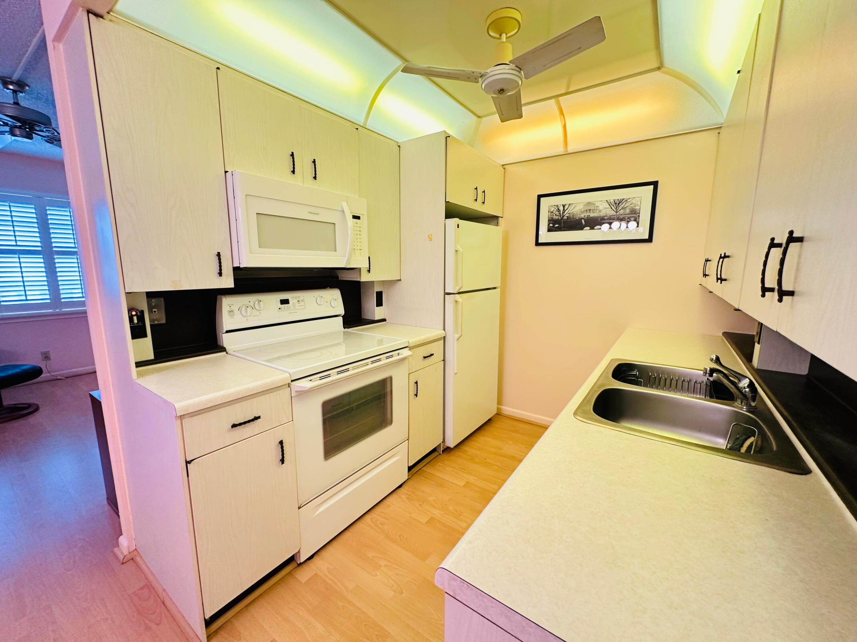 Kitchen featuring light-finish cabinetry, white appliances, integrated over-range microwave, double-basin stainless steel sink, and wood-finish flooring