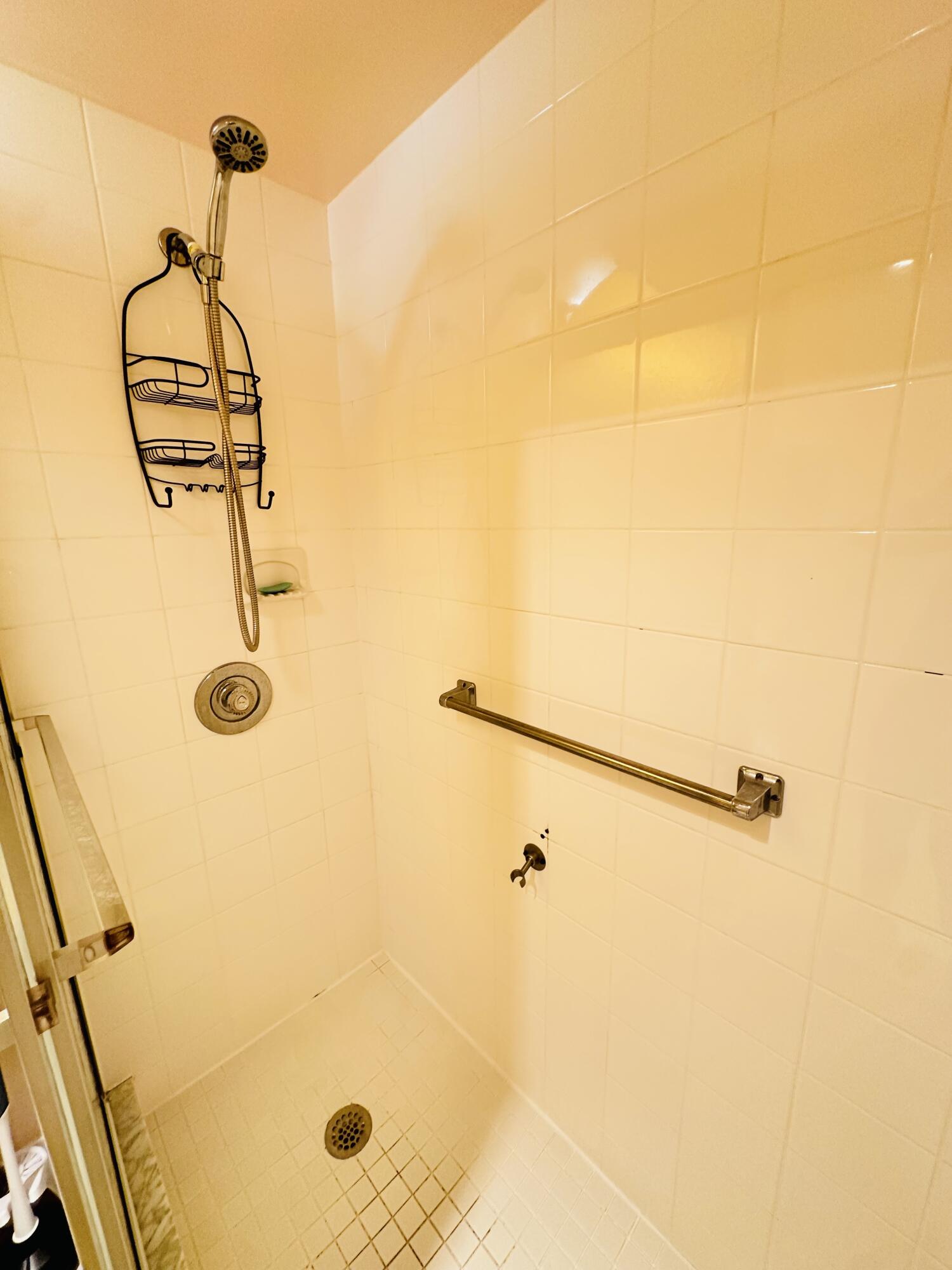 Walk-in shower featuring tiled wall surfacing, a detachable shower head, a built-in recessed shelf, and a horizontal grab bar