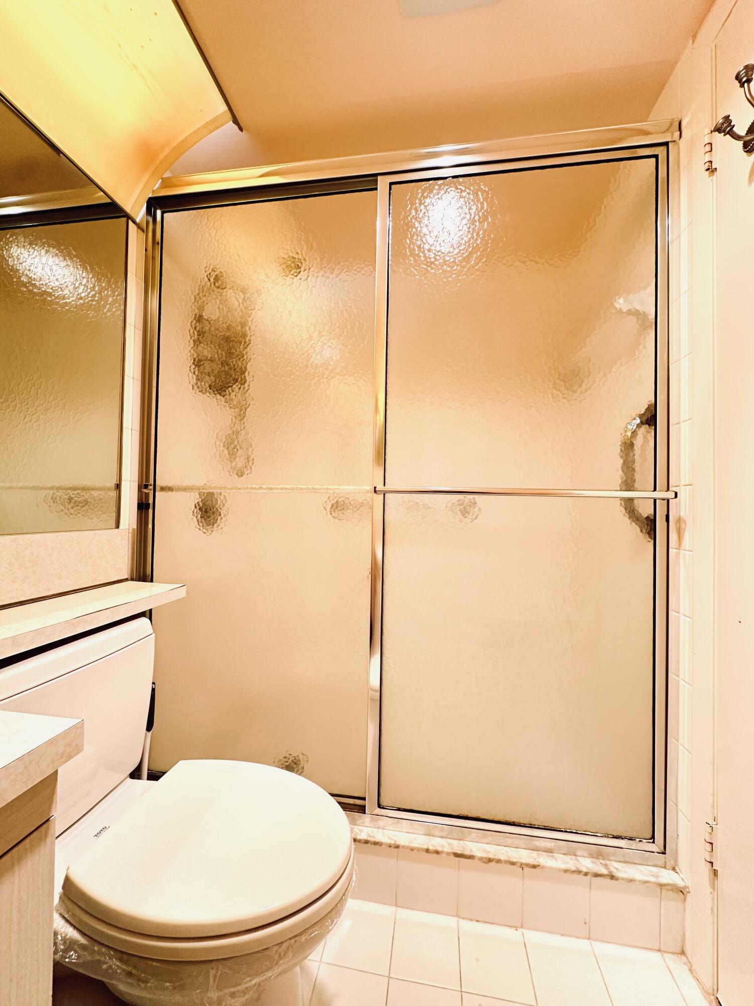 Walk-in shower enclosure featuring textured glass panels with polished metal framing, neutral tile flooring, and a solid-surface vanity countertop