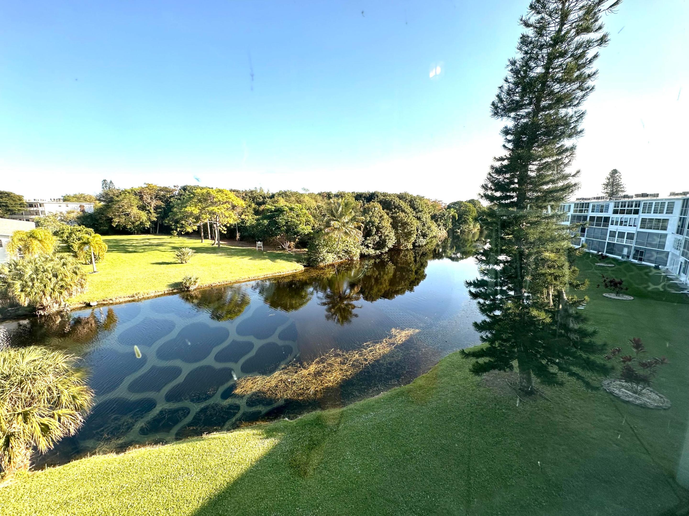 Waterfront setting featuring a pond, mature trees, and landscaped grounds
