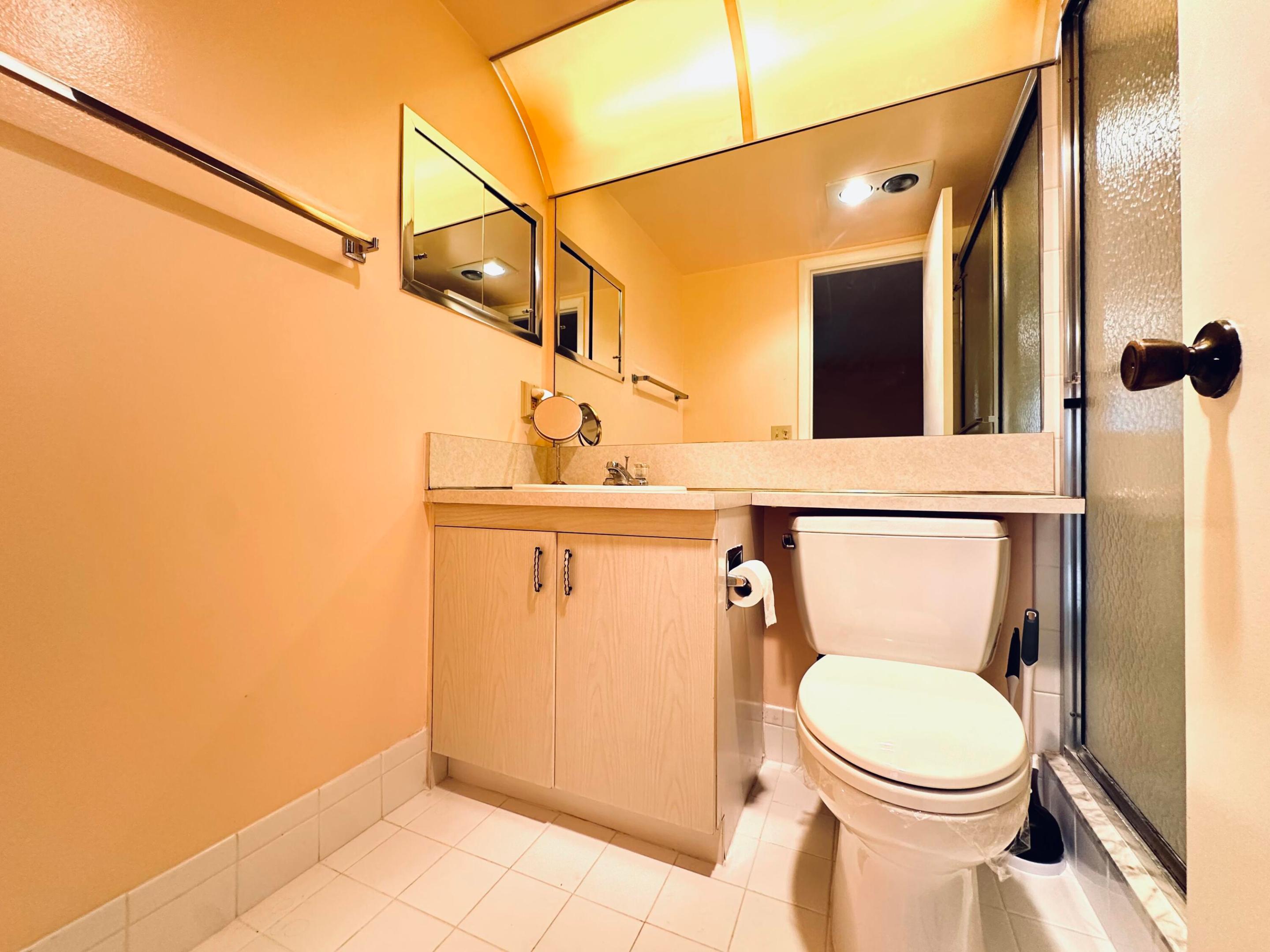 Bathroom vanity with integrated countertop and sink, wall-spanning vanity mirror, porcelain tile flooring, and a glass-enclosed shower stall