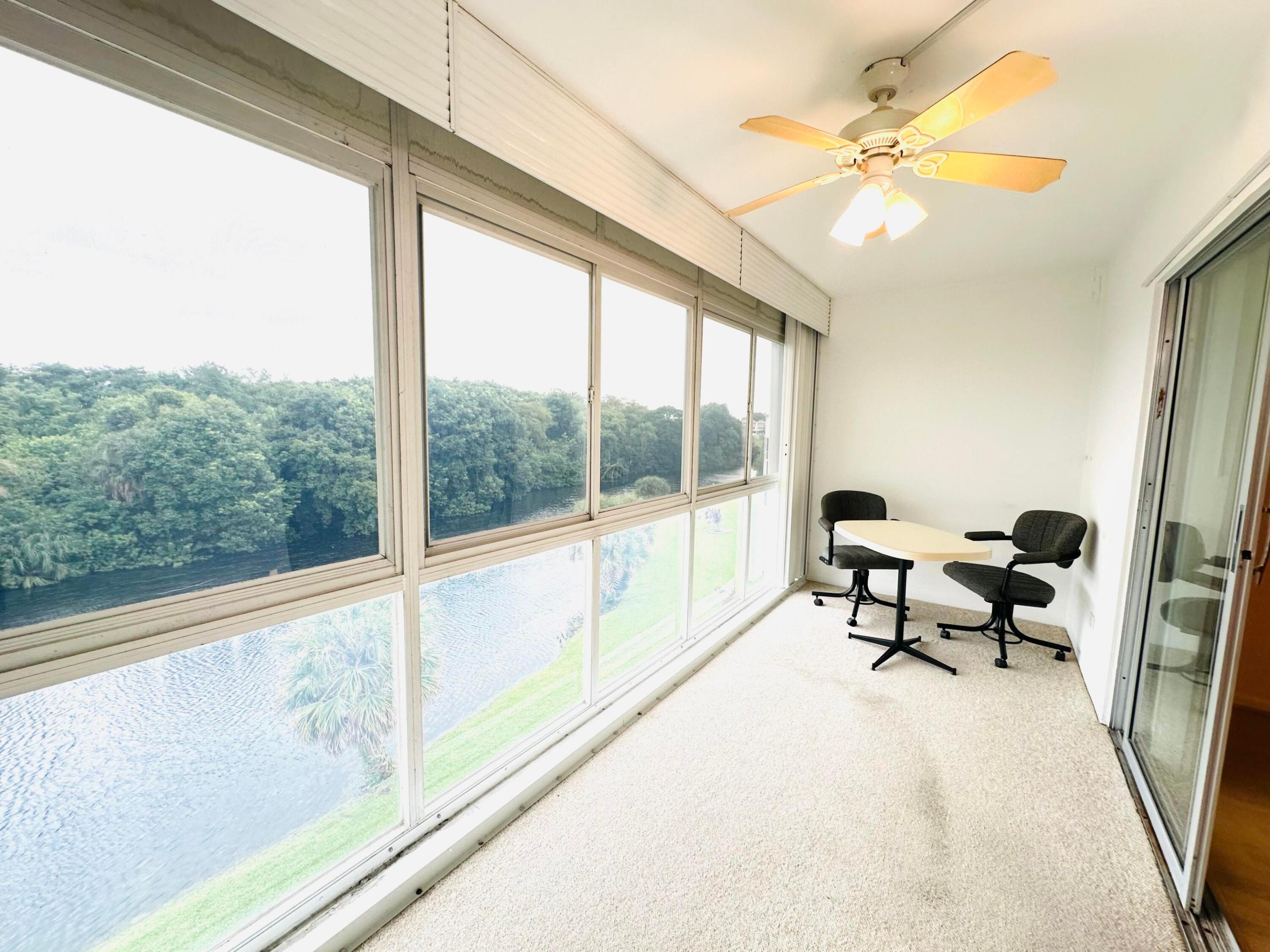 Enclosed sunroom featuring expansive floor-to-ceiling windows, water-facing exterior, textured flooring, and a ceiling-mounted light fixture with fan