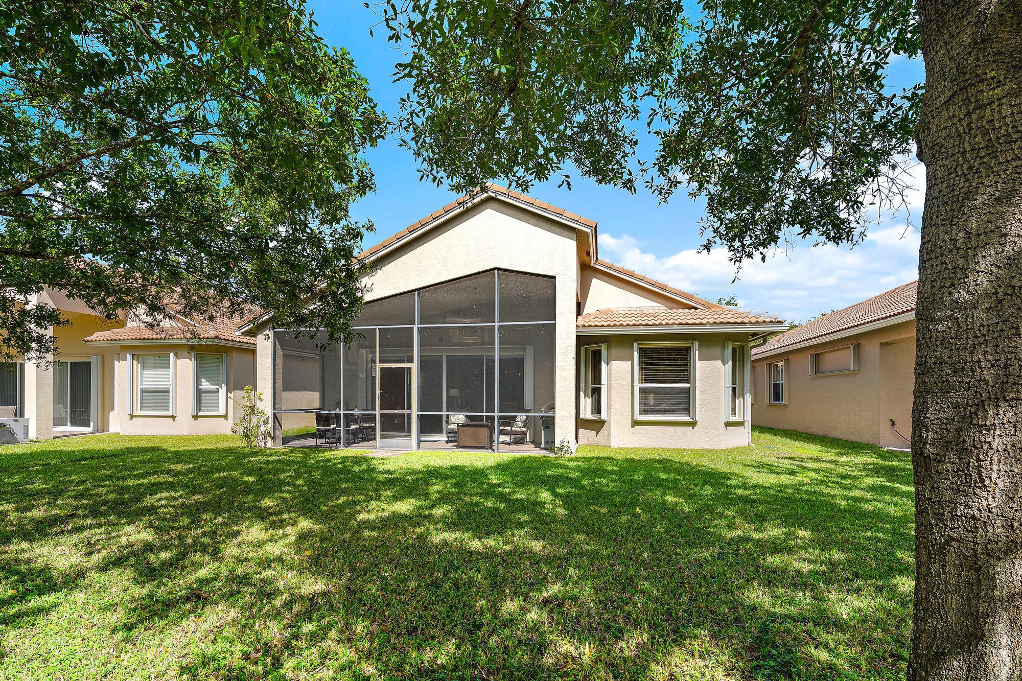 Stucco exterior featuring a screened-in lanai, concrete tile roof, and expansive lawn with mature trees