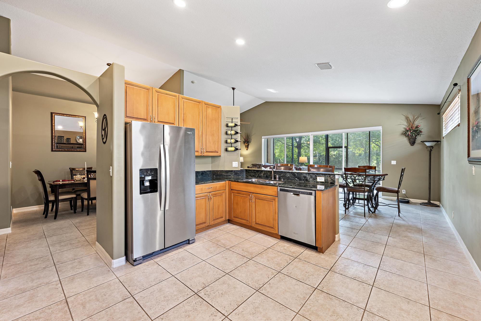 Kitchen featuring natural wood cabinetry, dark stone countertops, stainless steel appliances, tile flooring, and vaulted ceilings