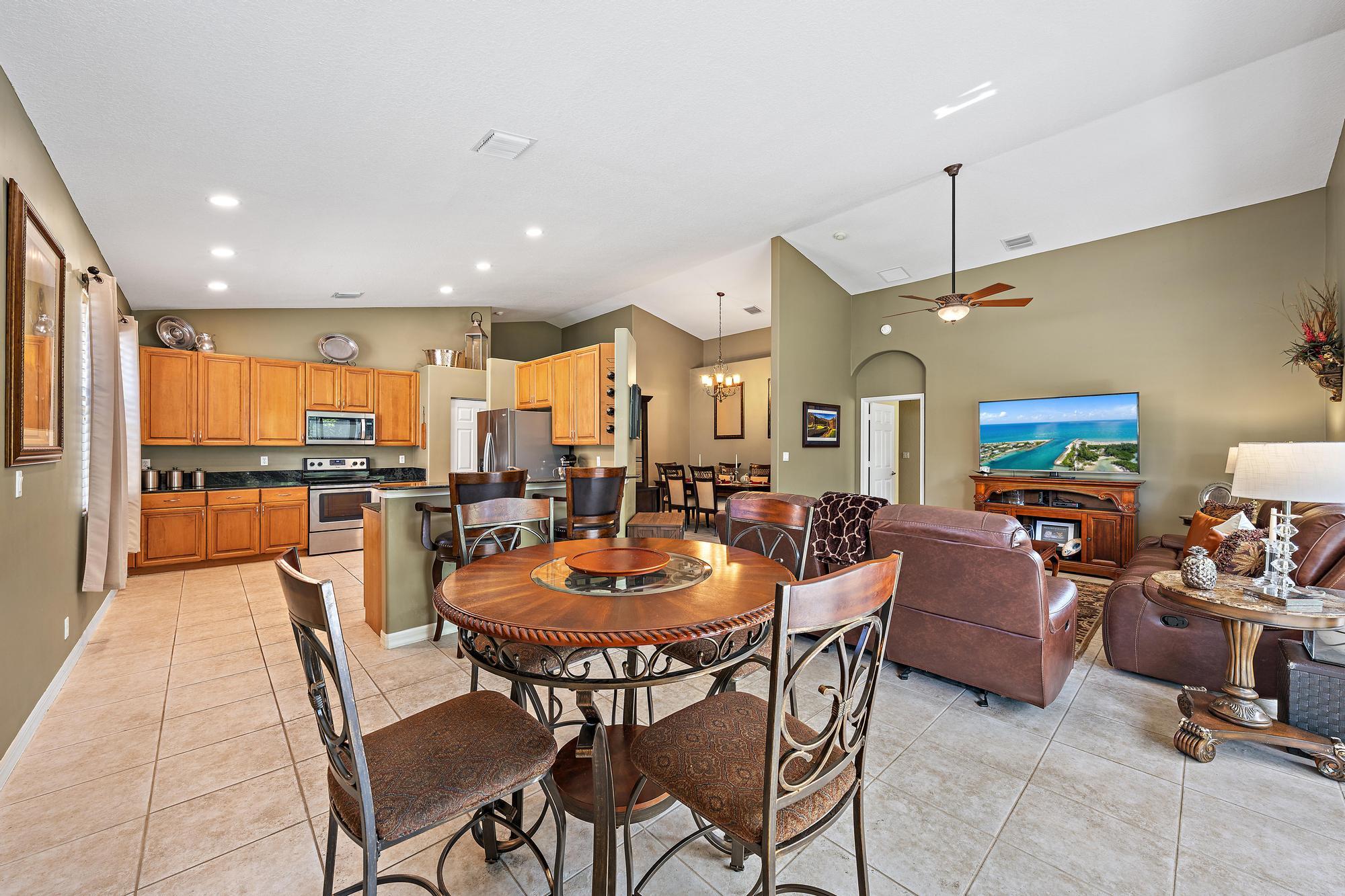 Open concept interior featuring vaulted ceilings, recessed lighting, tile flooring, and a kitchen equipped with wood cabinetry and a breakfast bar