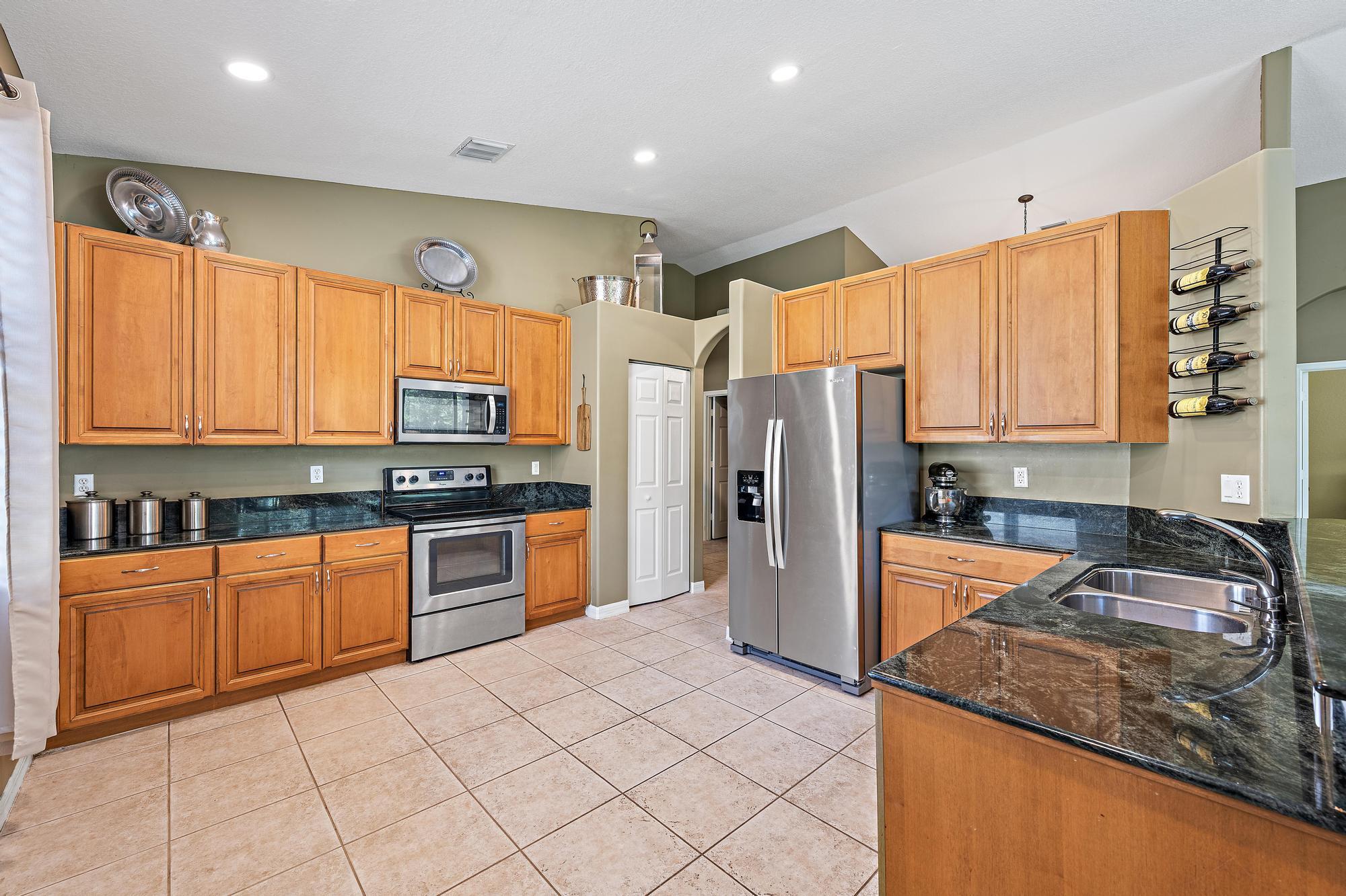 Kitchen featuring natural wood cabinetry, dark stone countertops, stainless steel appliances, a double-basin sink, and tile flooring