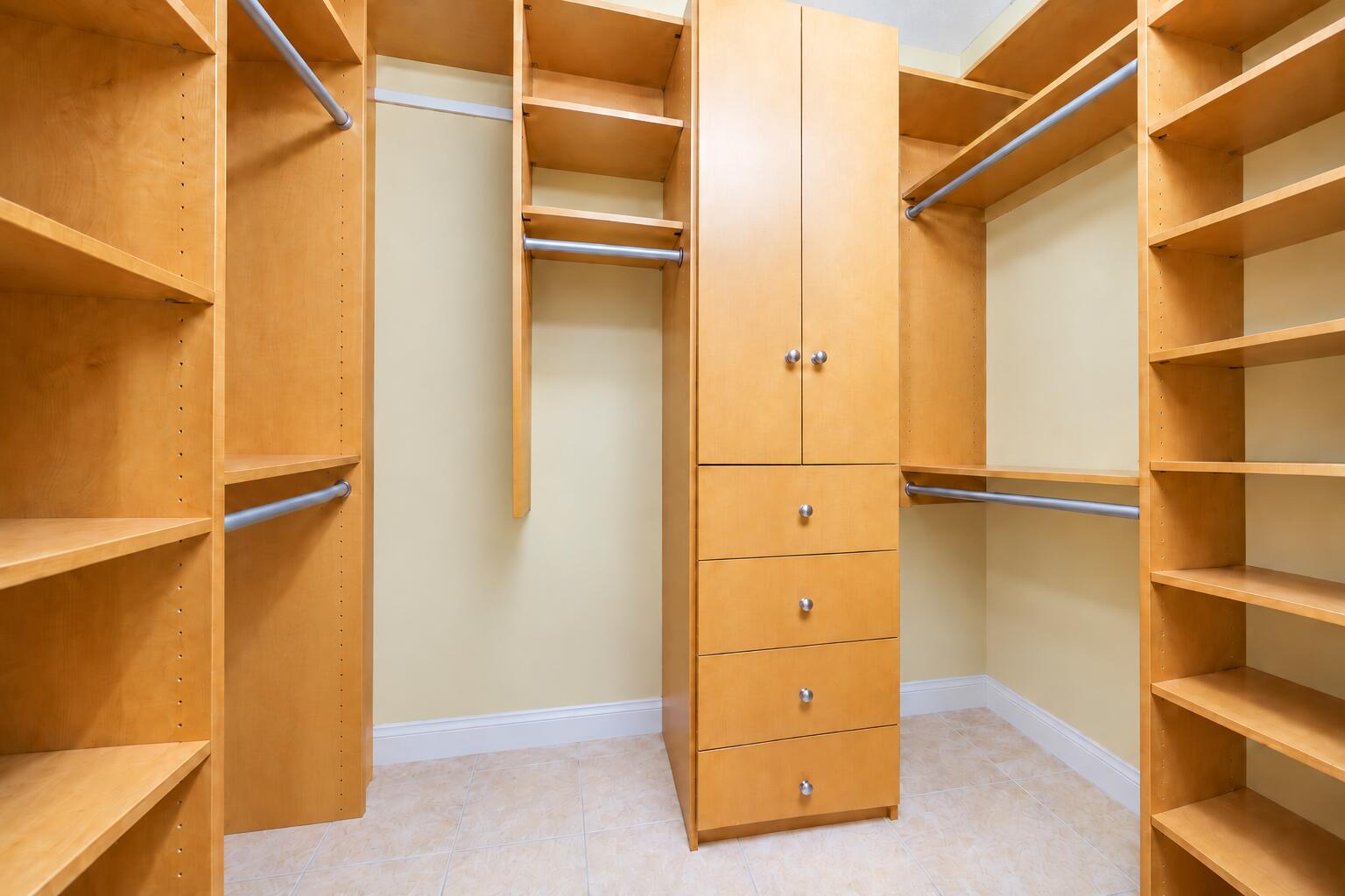 Custom walk-in closet featuring light-toned wood cabinetry, built-in drawer storage, adjustable shelving, and multi-tier hanging rods