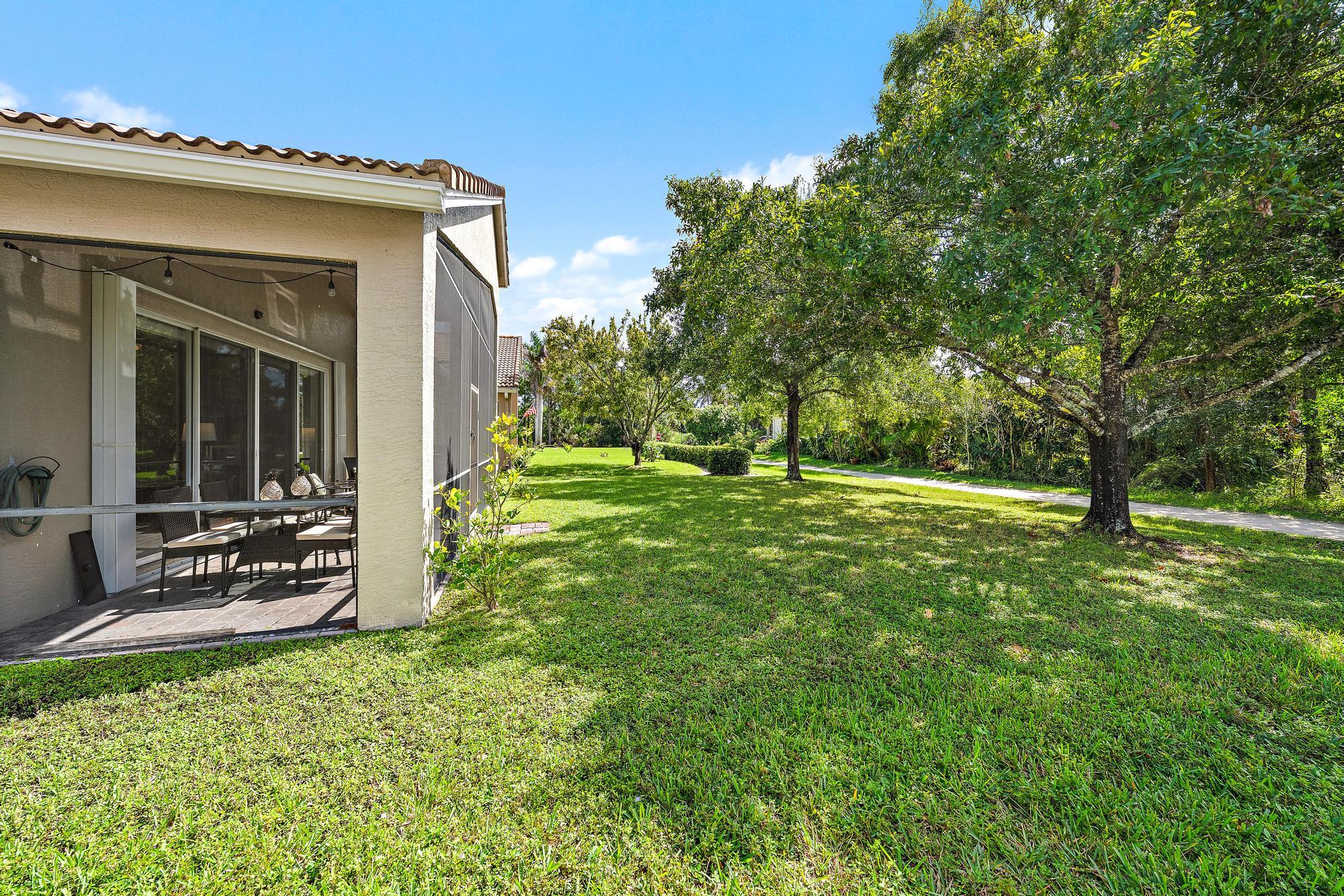 Screen-enclosed patio featuring a concrete floor, stucco exterior finish, sliding glass doors, and a spacious lawn with mature shade trees