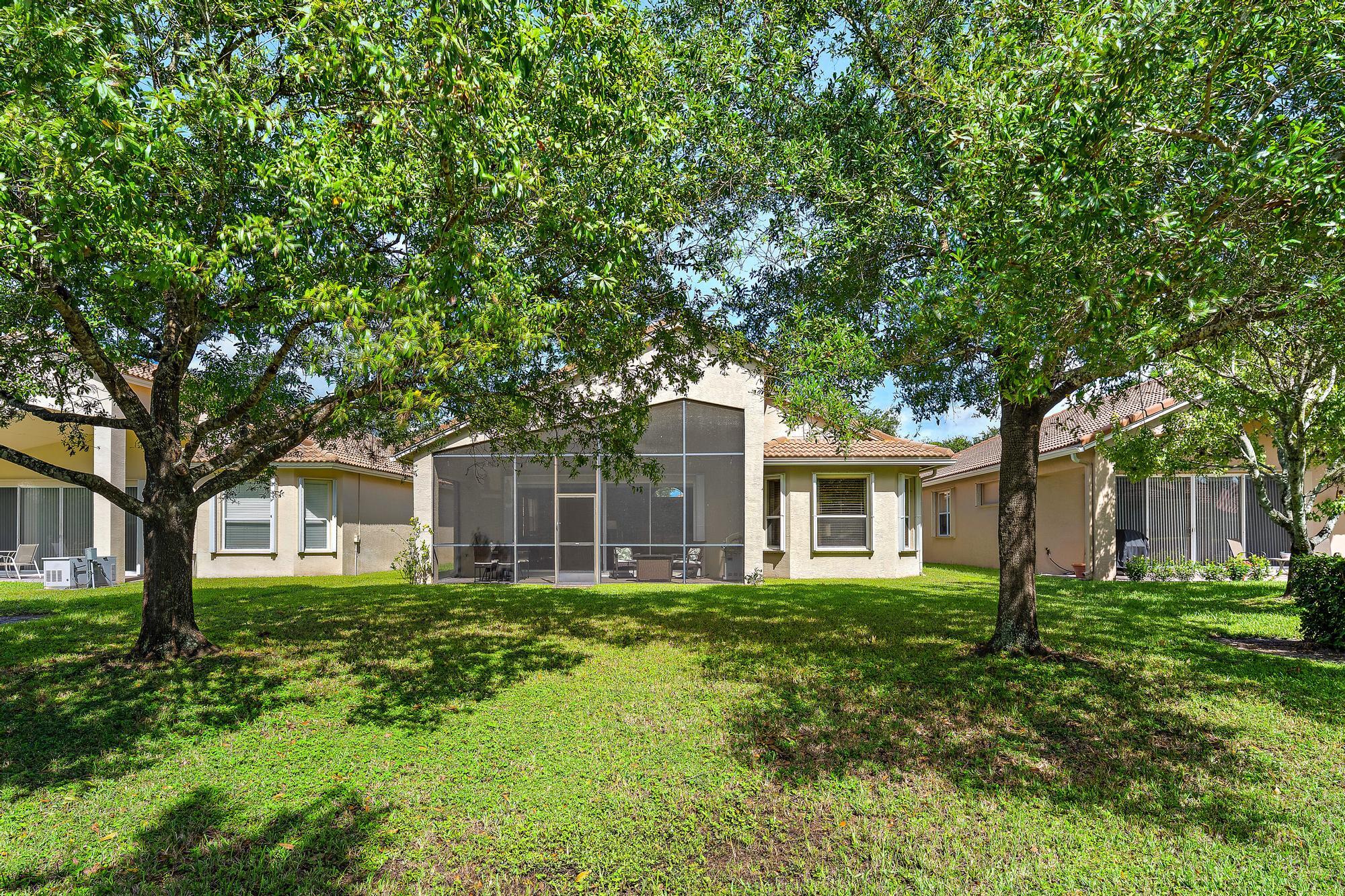 Stucco exterior with a screened-in lanai, manicured lawn, and mature canopy trees